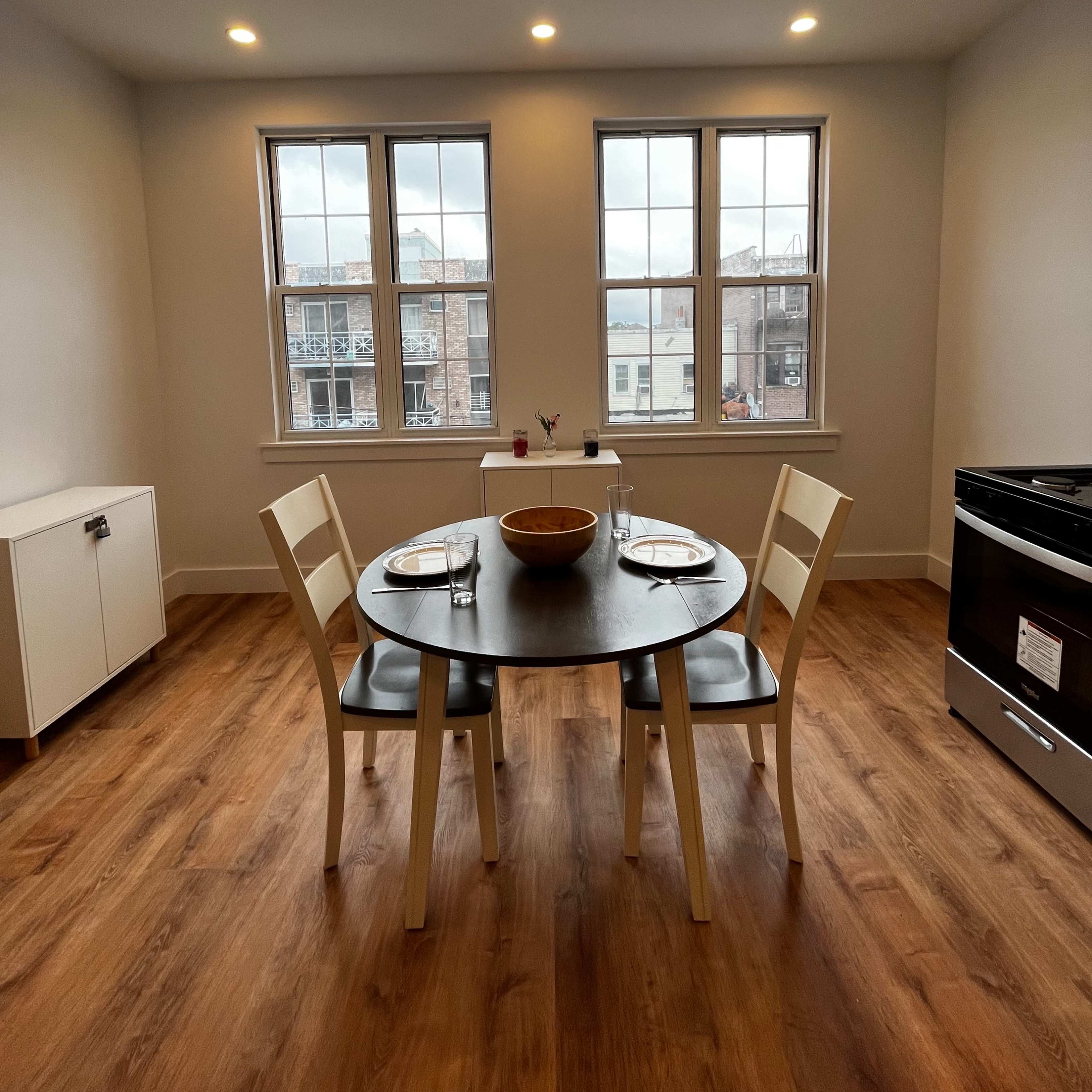 A kitchen space featuring a round table set for two, with a bowl at the center, two chairs, and a stove in the corner.