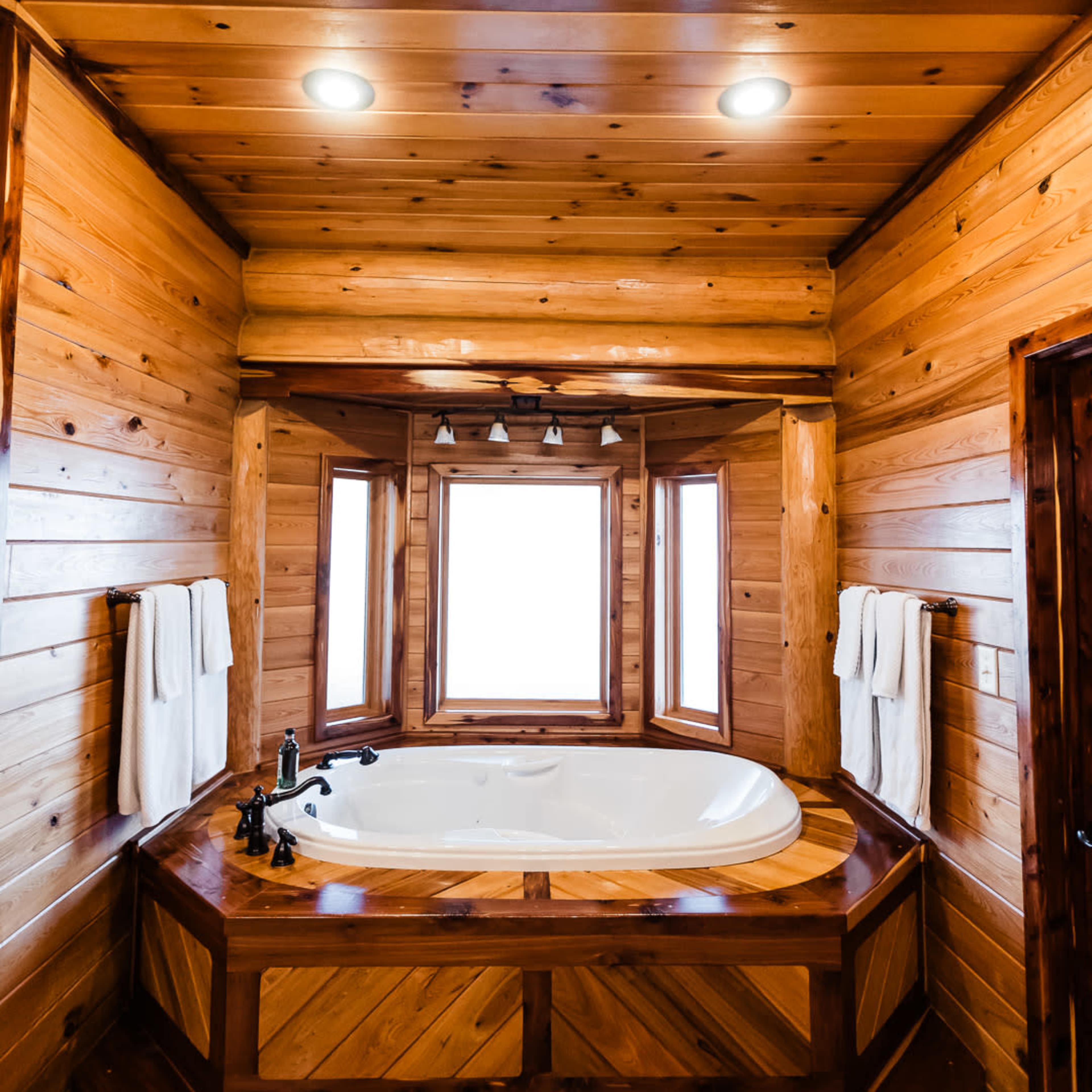 A wooden bathroom featuring a large, round bathtub surrounded by windows and accented by wooden walls and decor.