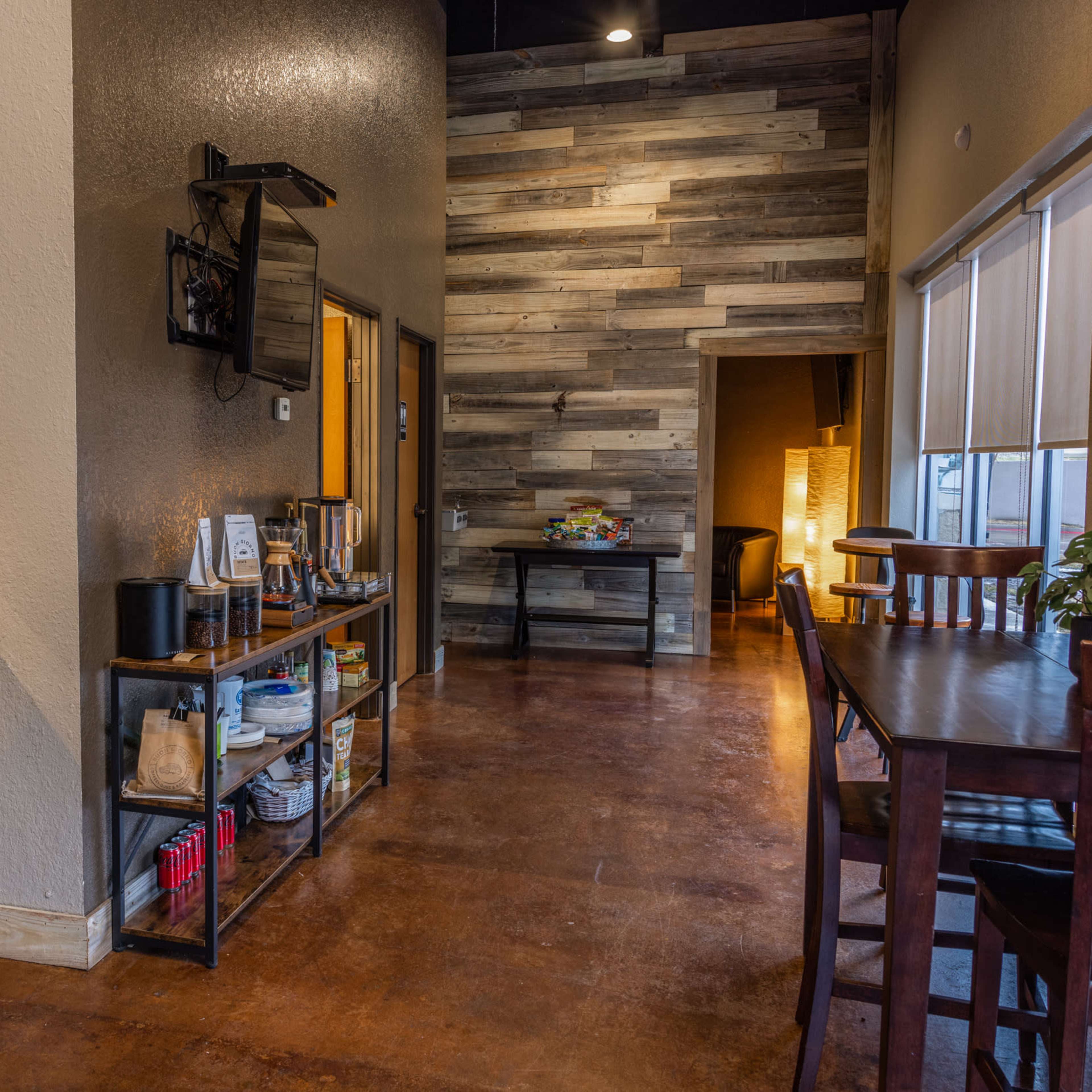 A modern kitchen area features stainless steel appliances and a shelf with various items, adjacent to a wooden-paneled wall and a dining area.