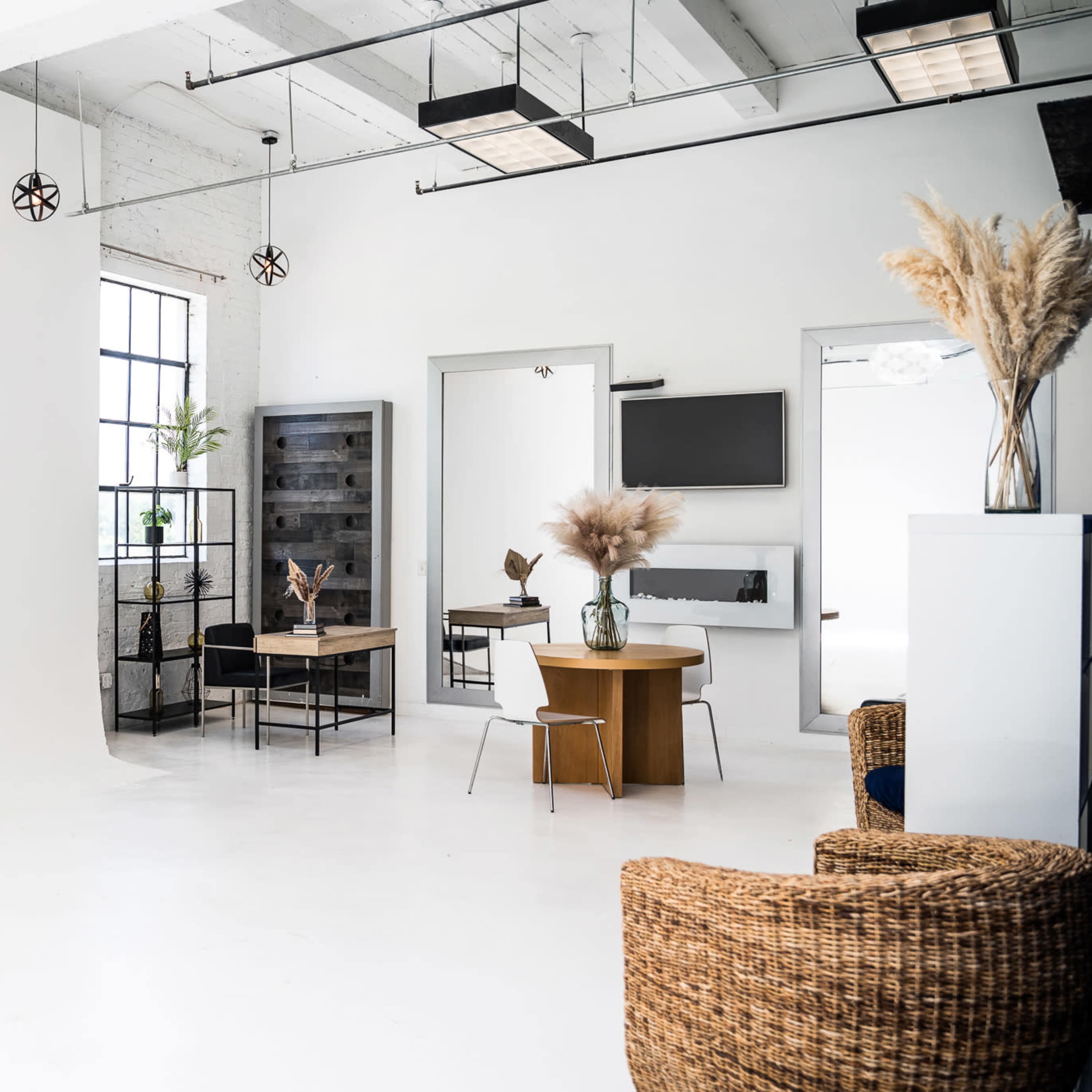 A bright, minimalist studio space with a large window, a wooden table, a black chair, and decorative plants.