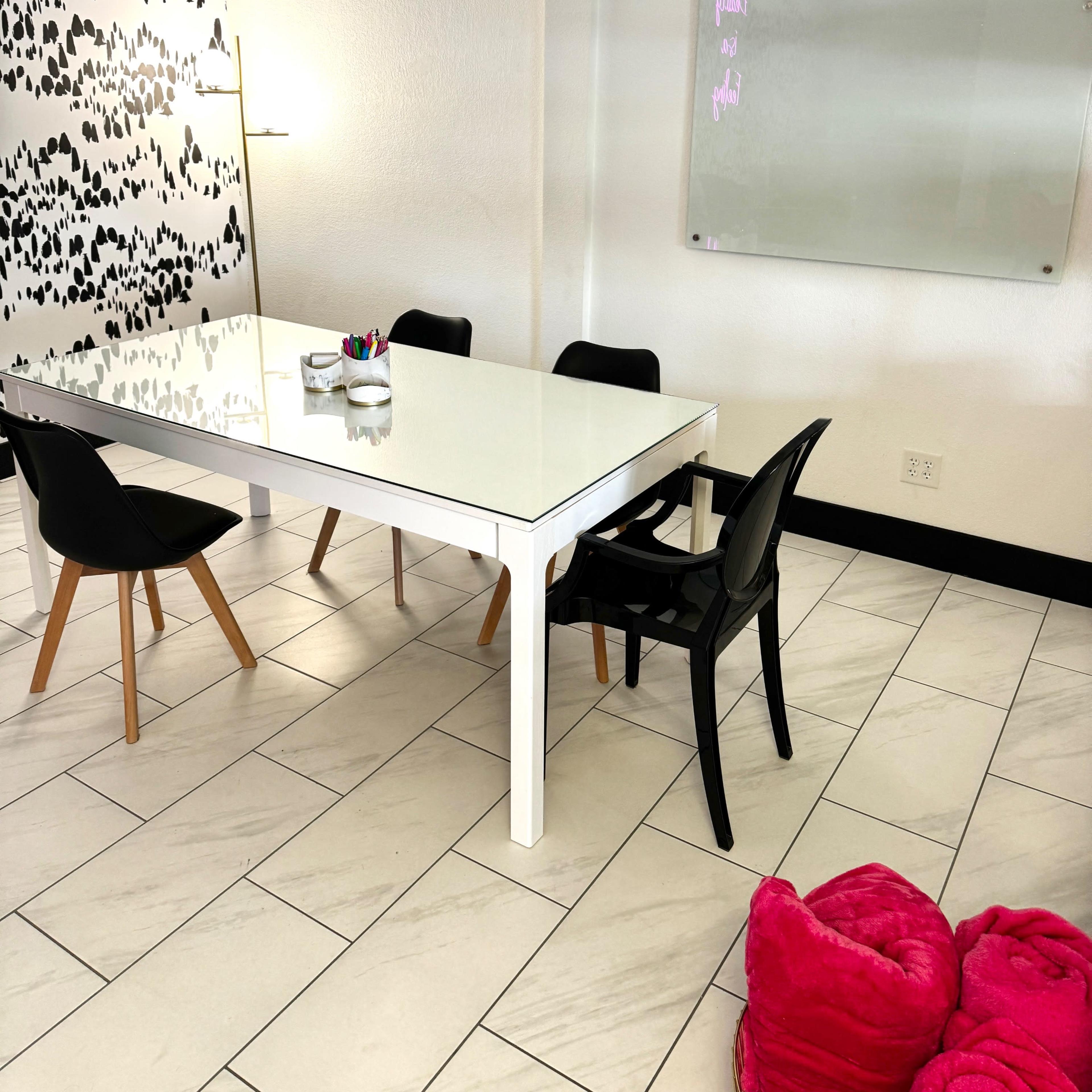 A modern meeting room features a white table surrounded by black chairs, with a patterned wall and a glass whiteboard.