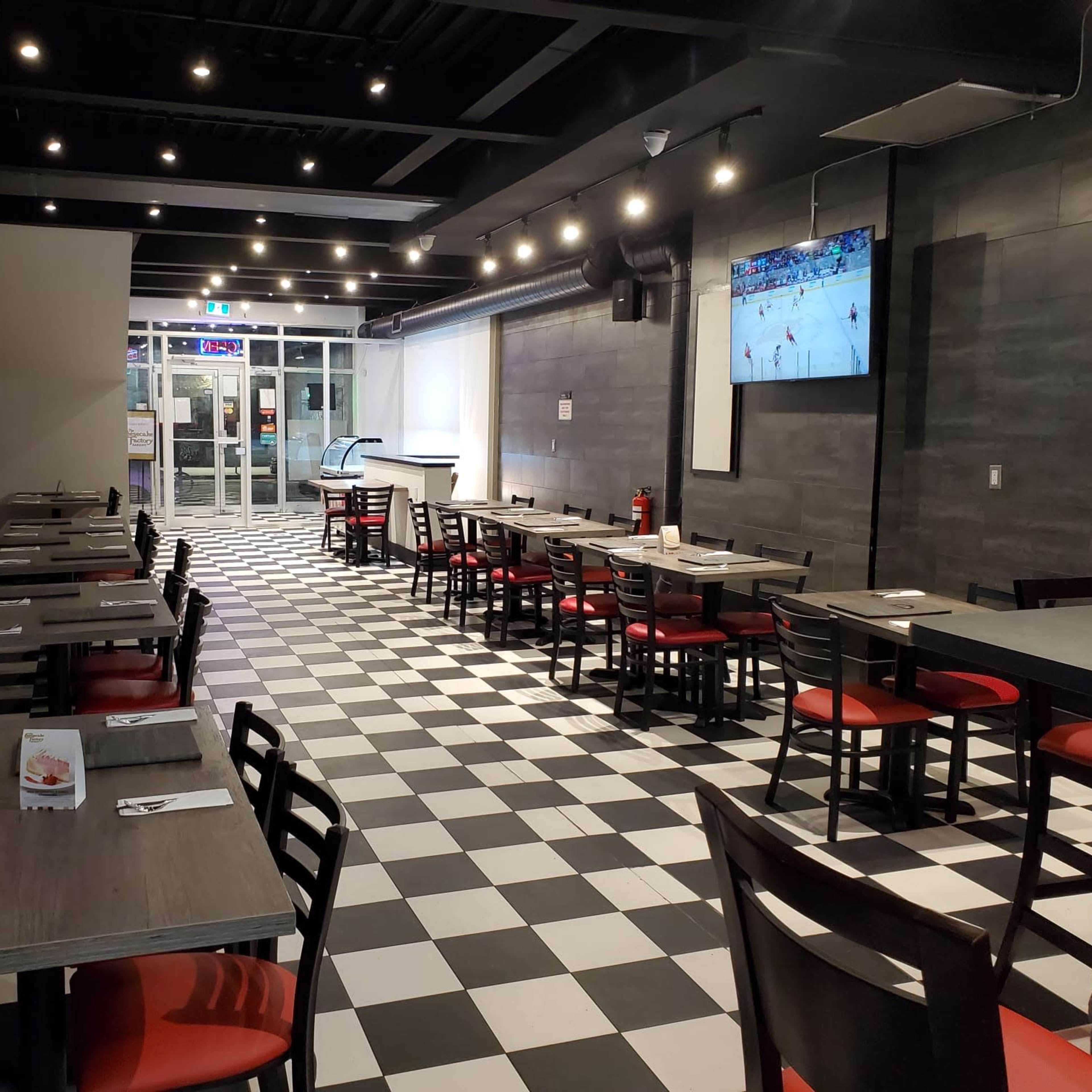 A modern restaurant interior with checkered flooring, red and black seating, and two televisions mounted on the walls.