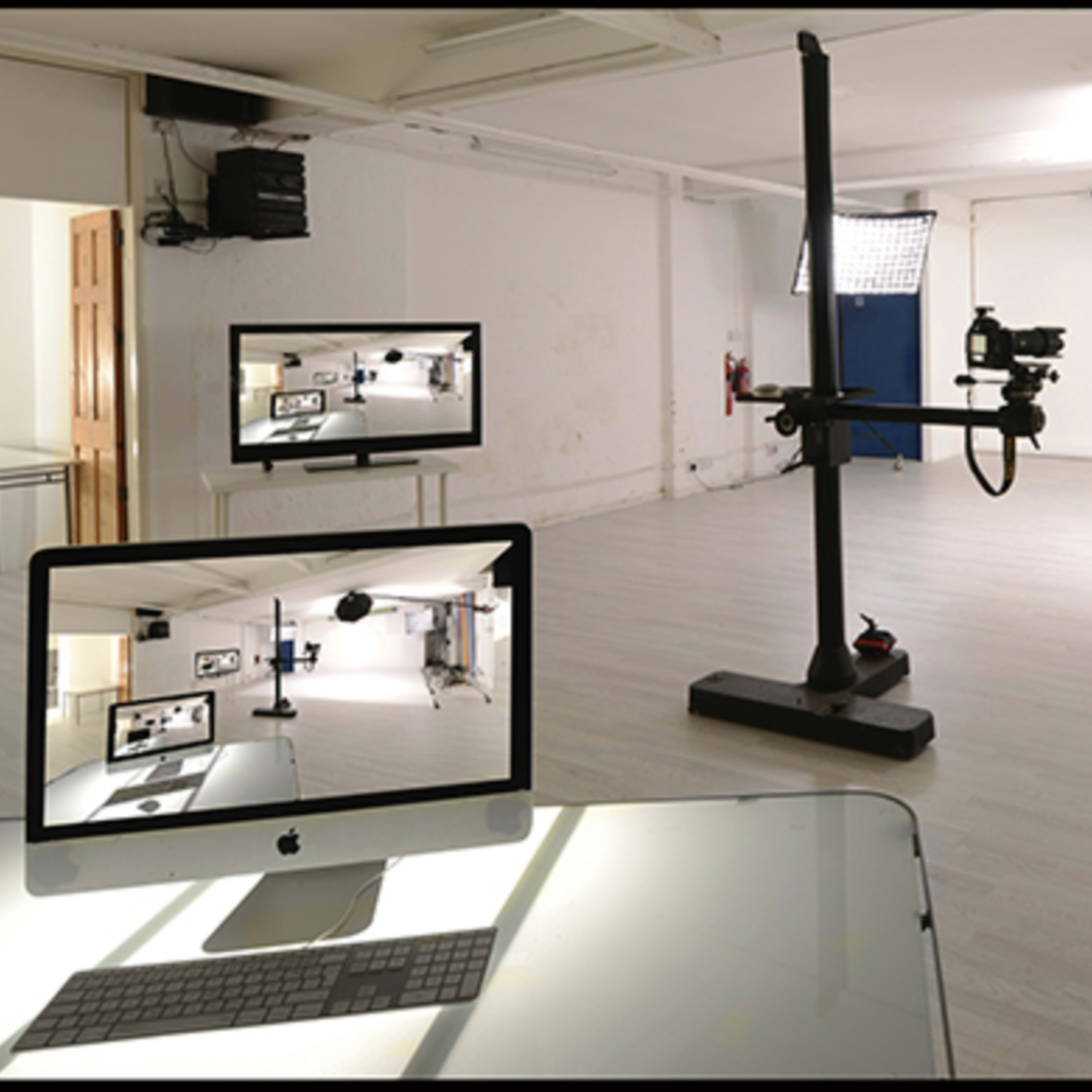 A photography studio is equipped with lighting equipment, a camera on a stand, and a computer displaying a live feed of the space.