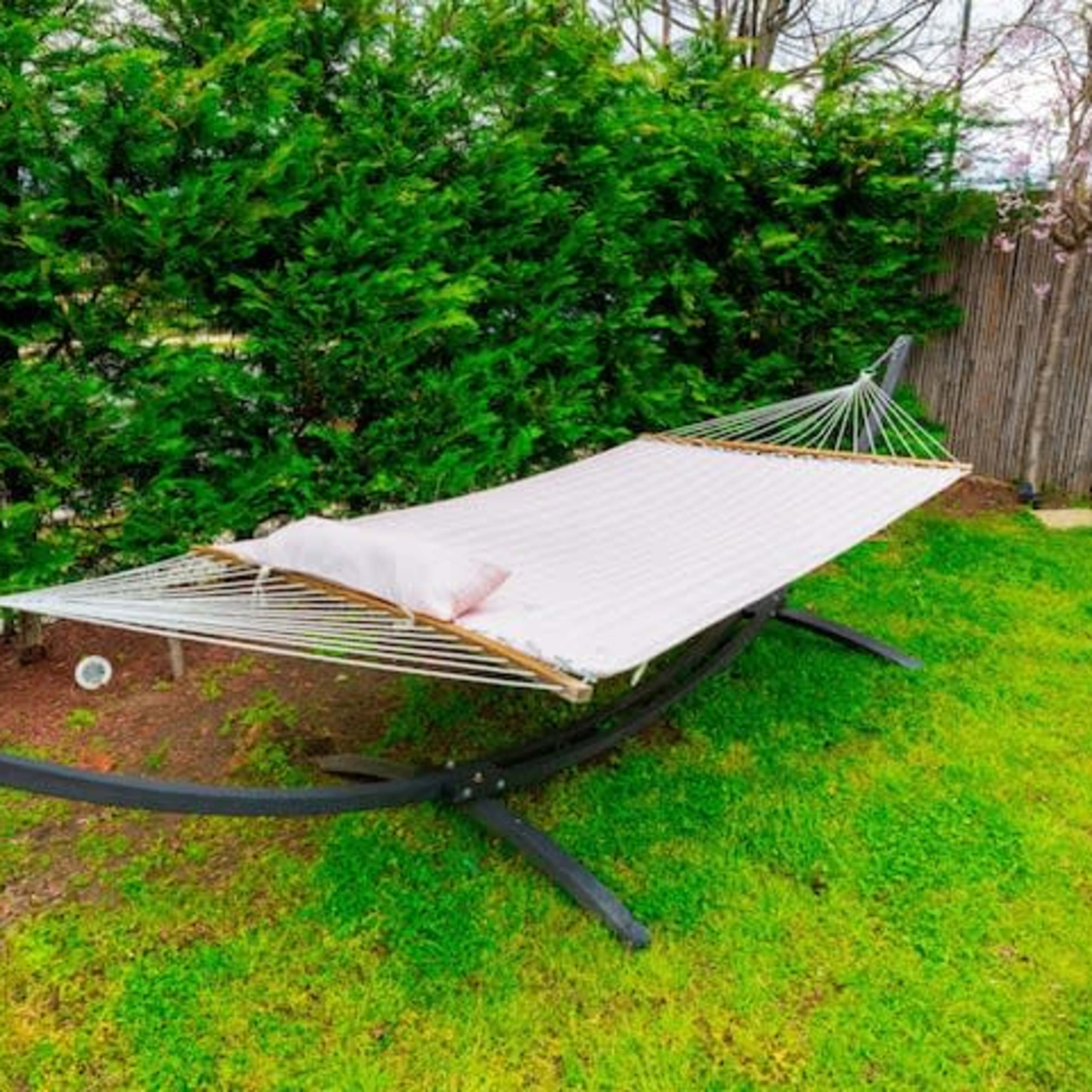 A hammock is suspended between two supports on grassy ground surrounded by shrubs.