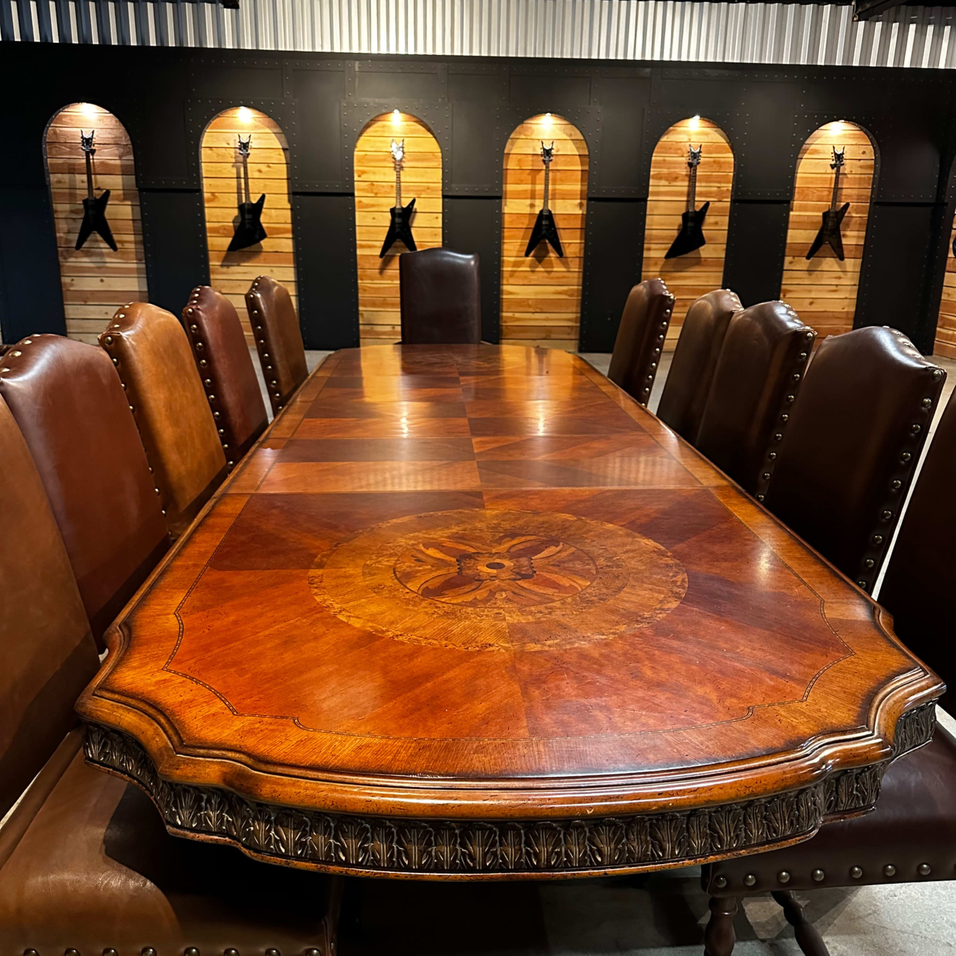 A large, ornate wooden conference table surrounded by leather chairs, set against a backdrop of wooden panels with mounted objects.