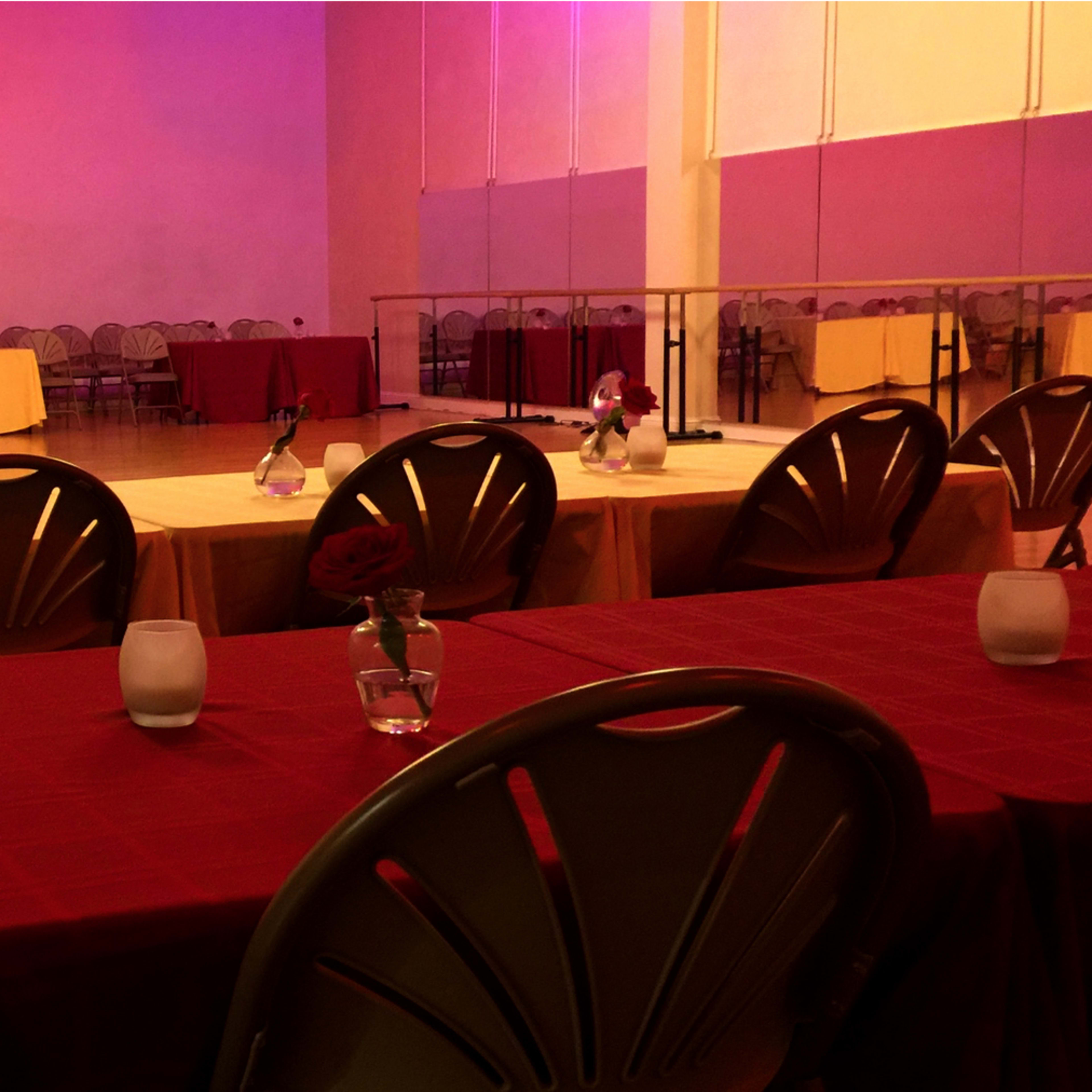 A dance studio with tables set in rows, some covered with red and yellow tablecloths, and chairs arranged around them.
