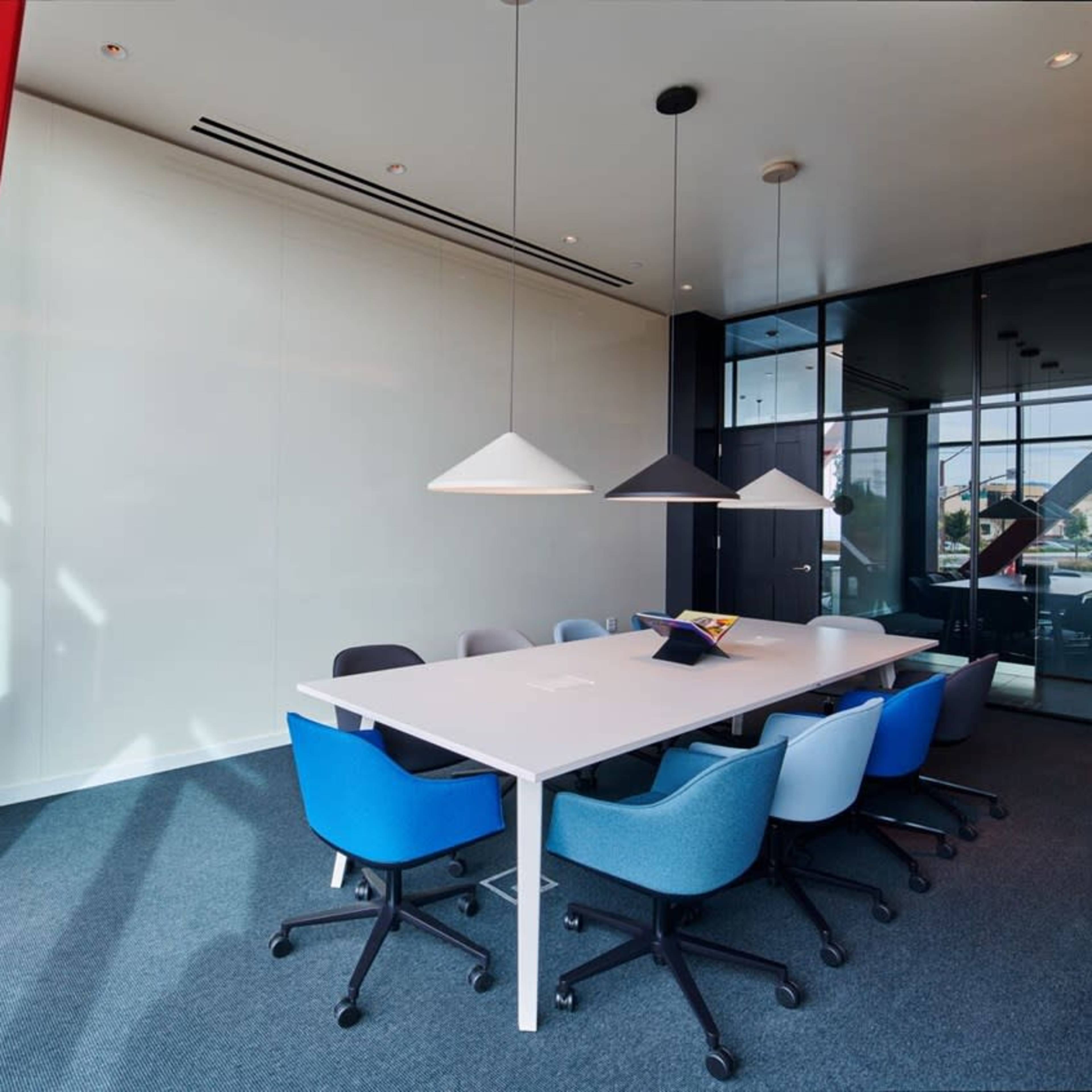 A modern conference room with a white table surrounded by colorful chairs and pendant lighting.