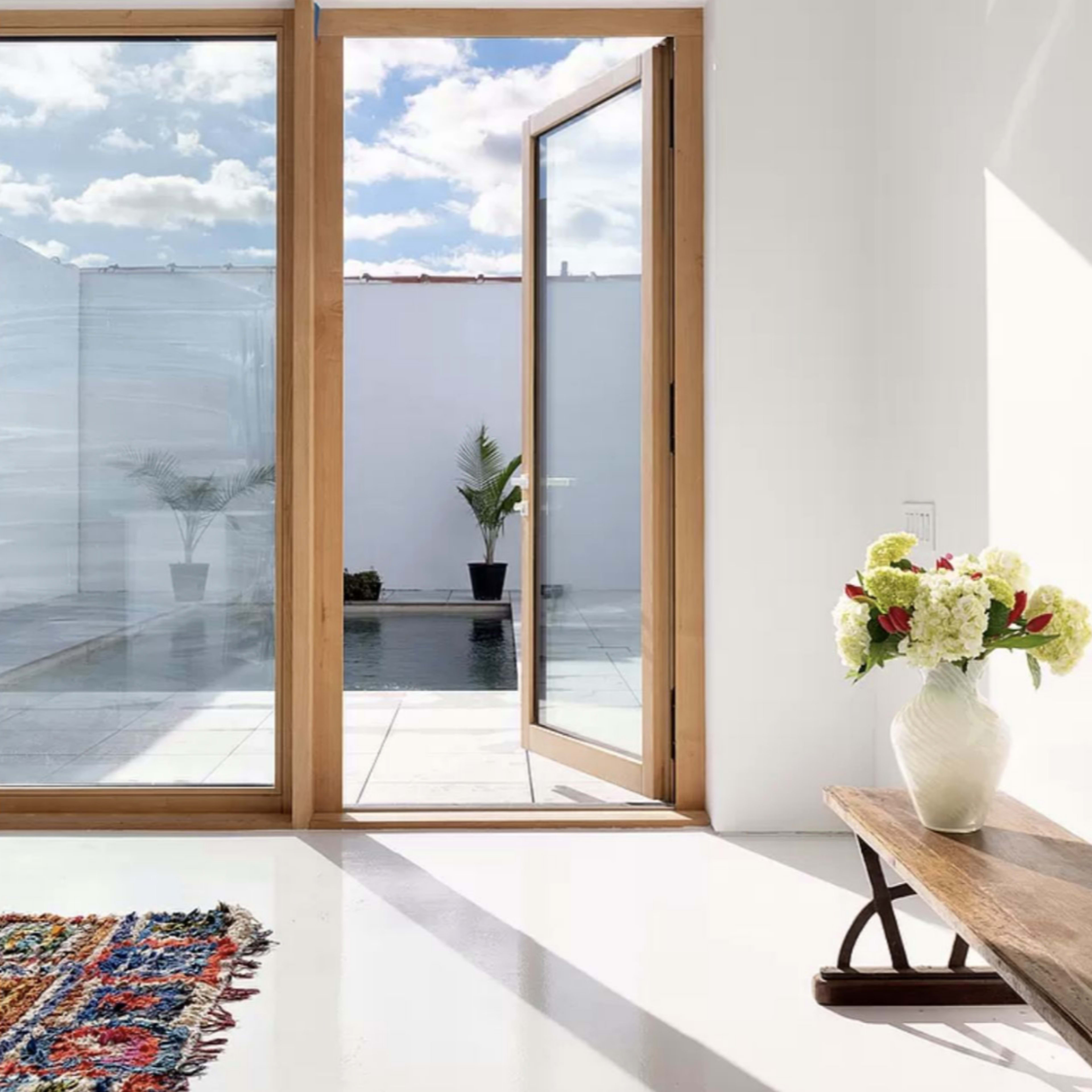 A spacious interior features large glass doors opening to a small pool area with potted plants.