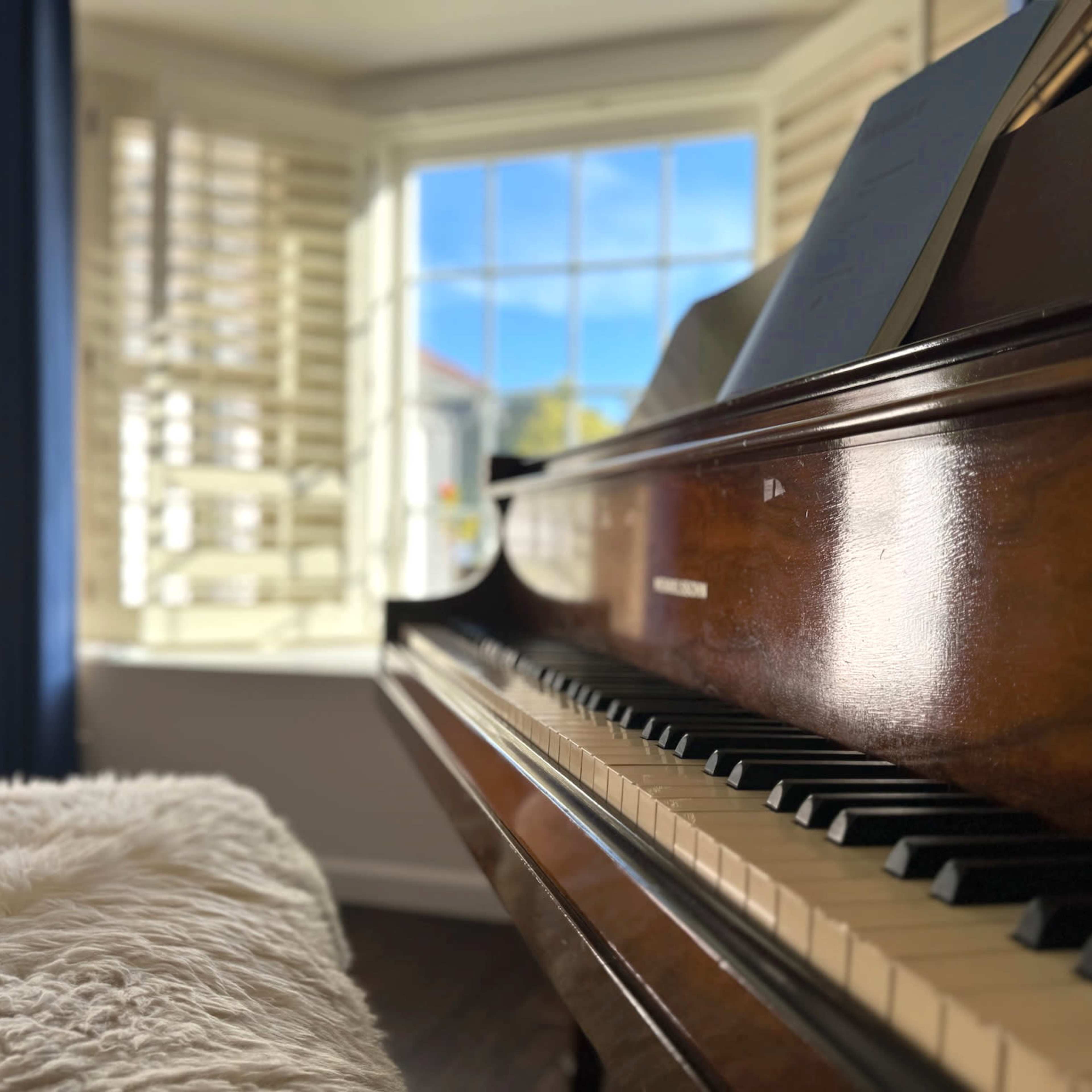 A close-up view of a polished piano keyboard with a sunny window and shutters in the background.