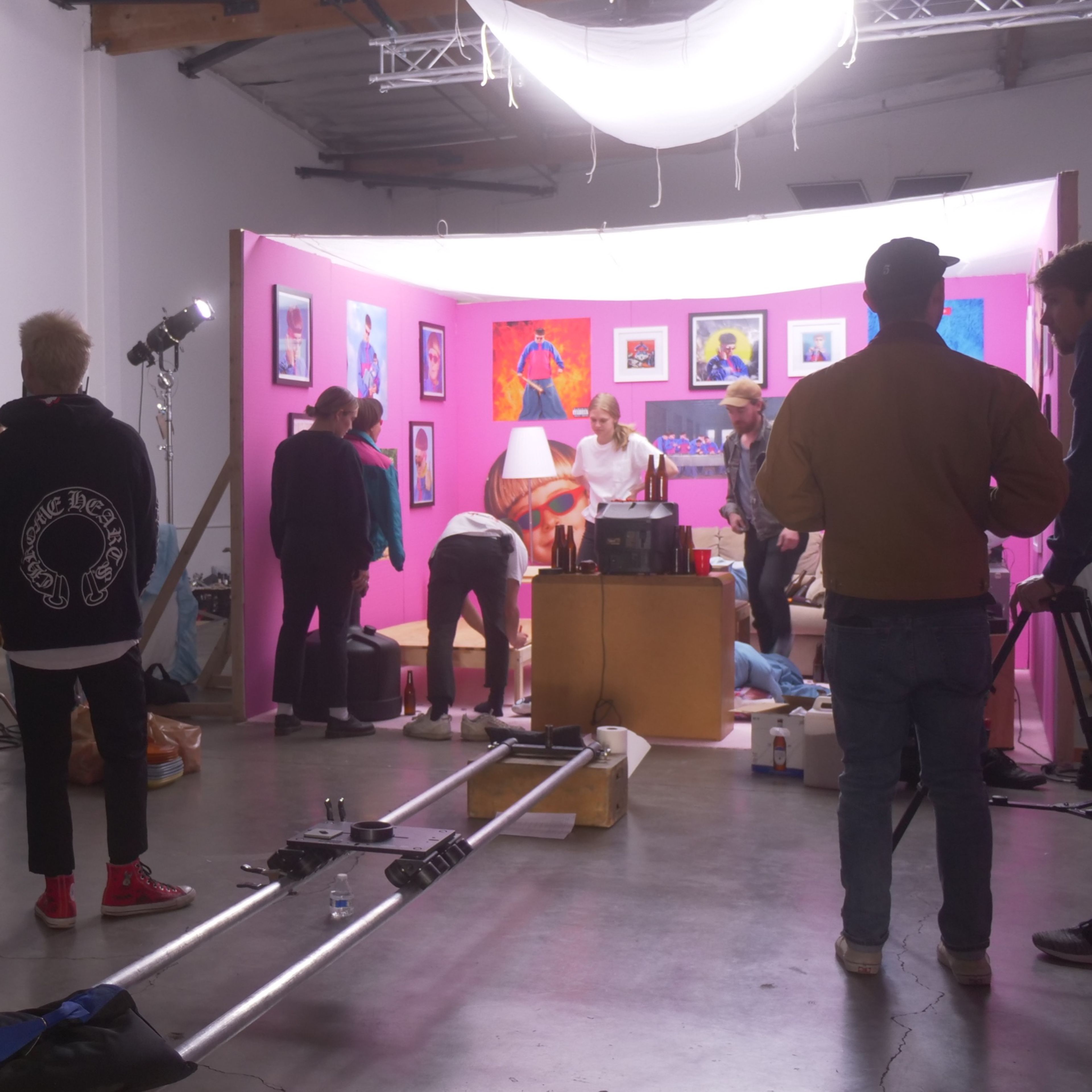 A group of people gathers in a studio space with a pink set design, preparing for a photoshoot or filming.