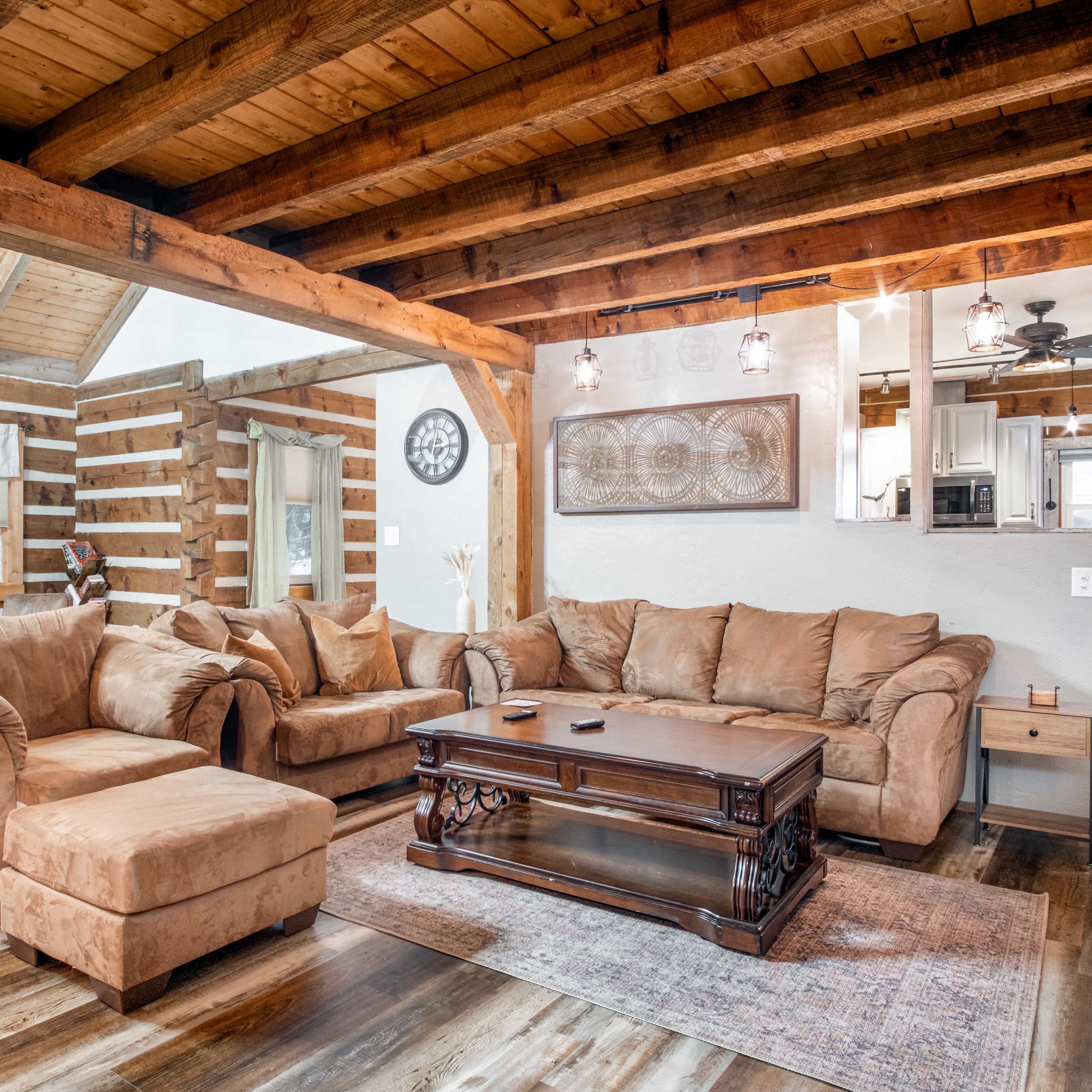 A spacious living room features a sectional sofa, a wooden coffee table, and exposed wooden beams in the ceiling.
