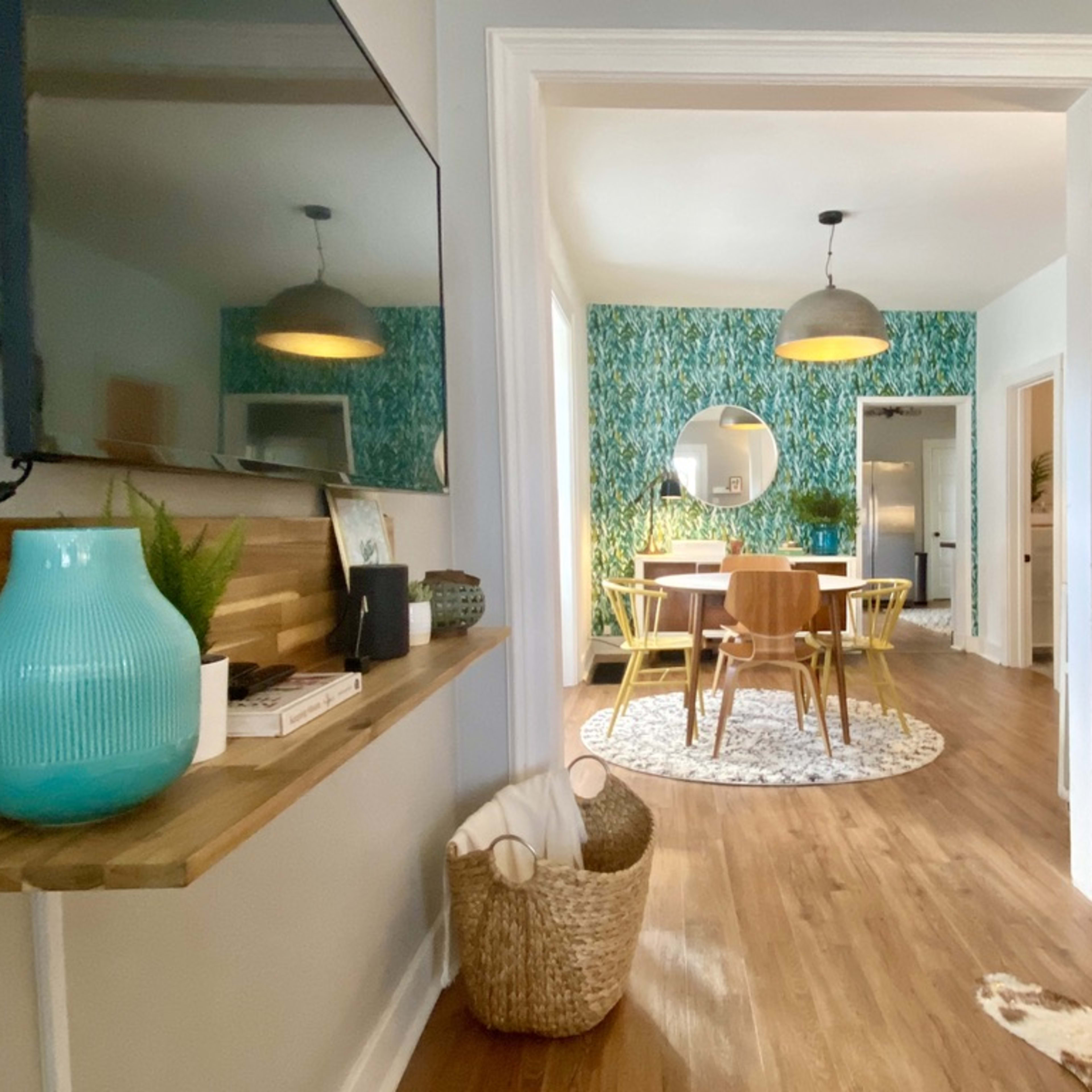 A view through an archway reveals a dining area with a round table and a colorful wallpaper backdrop.
