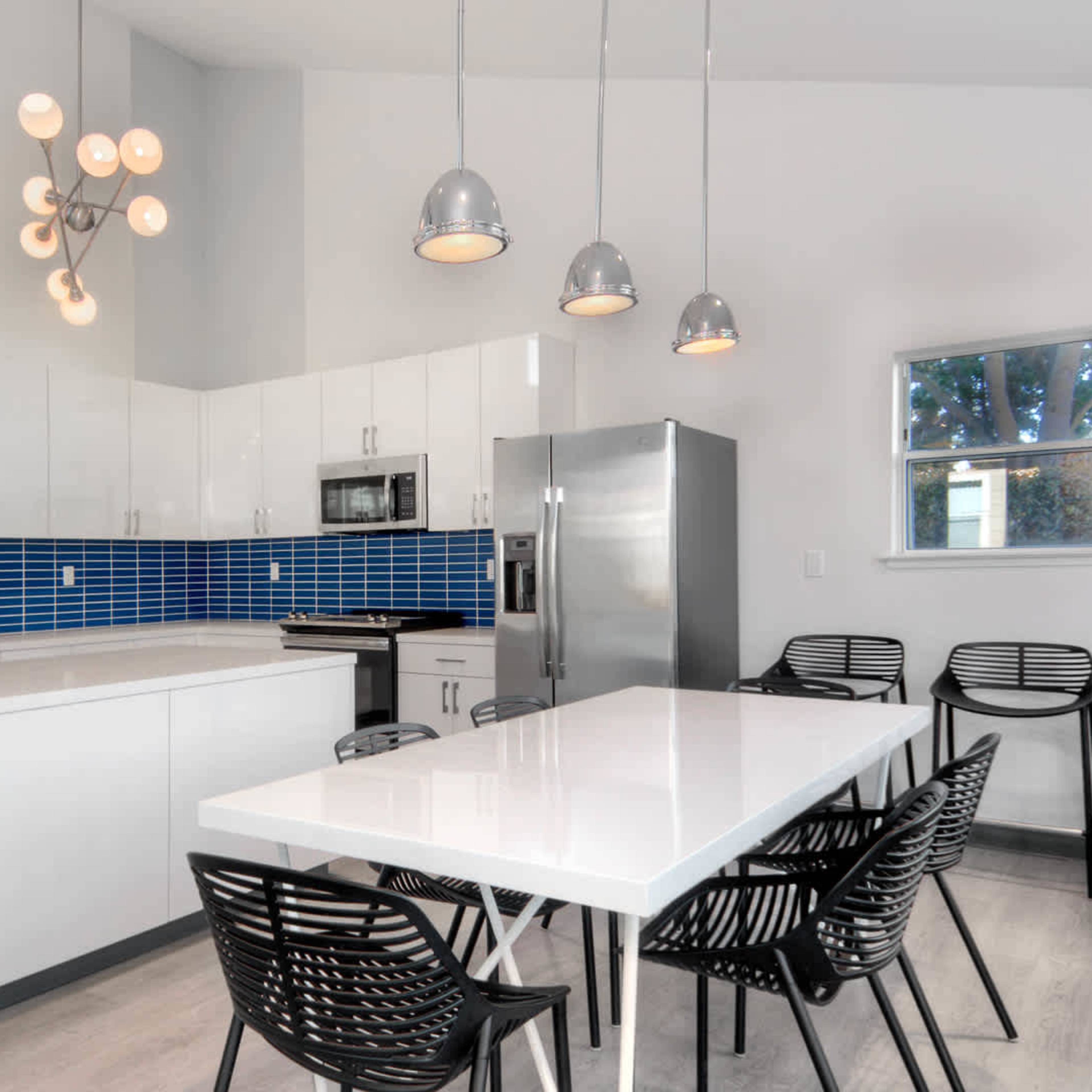A modern kitchen with a blue tiled backsplash, white cabinets, a large island, and a dining table with black chairs.