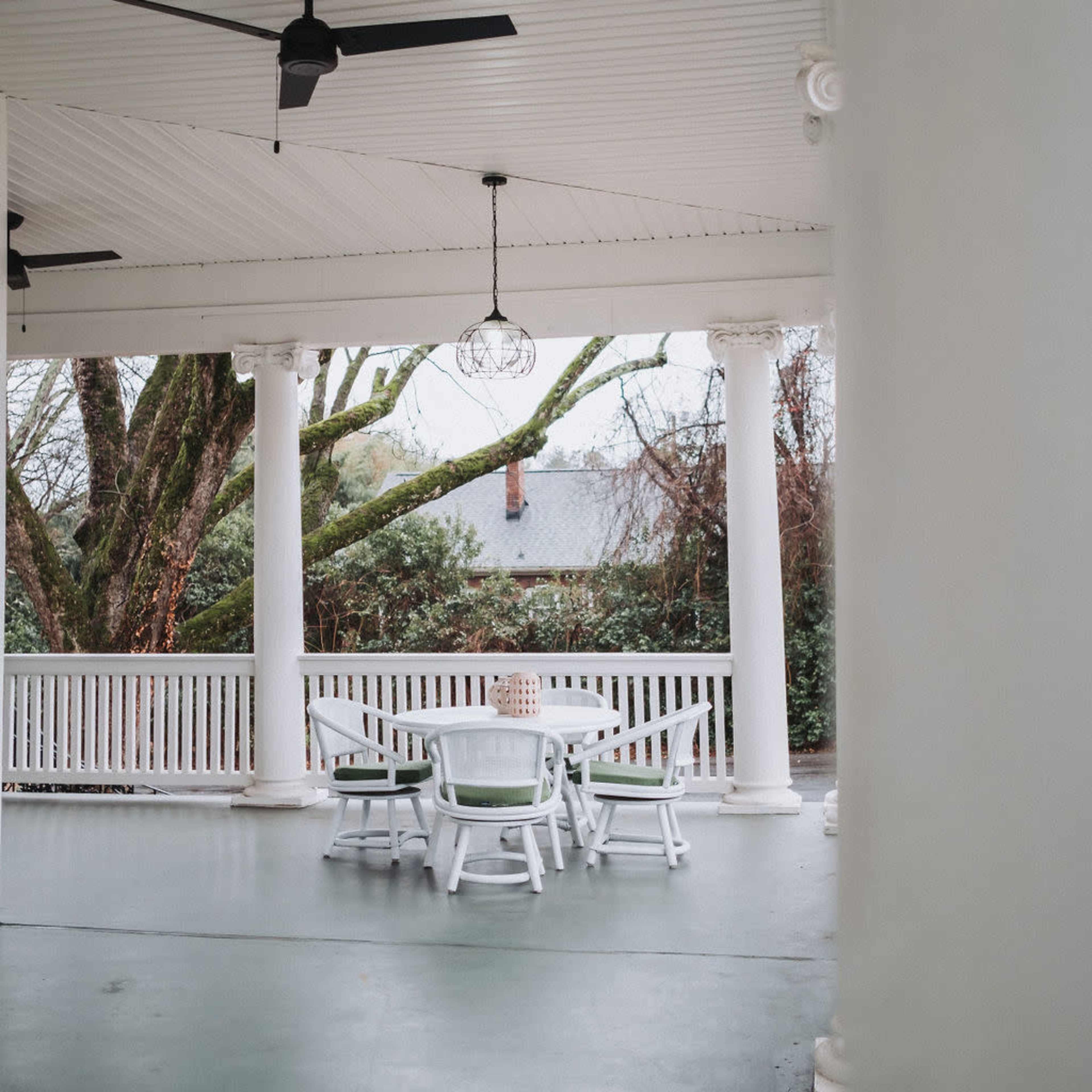 A covered porch with white columns and a round table surrounded by chairs overlooks a garden.