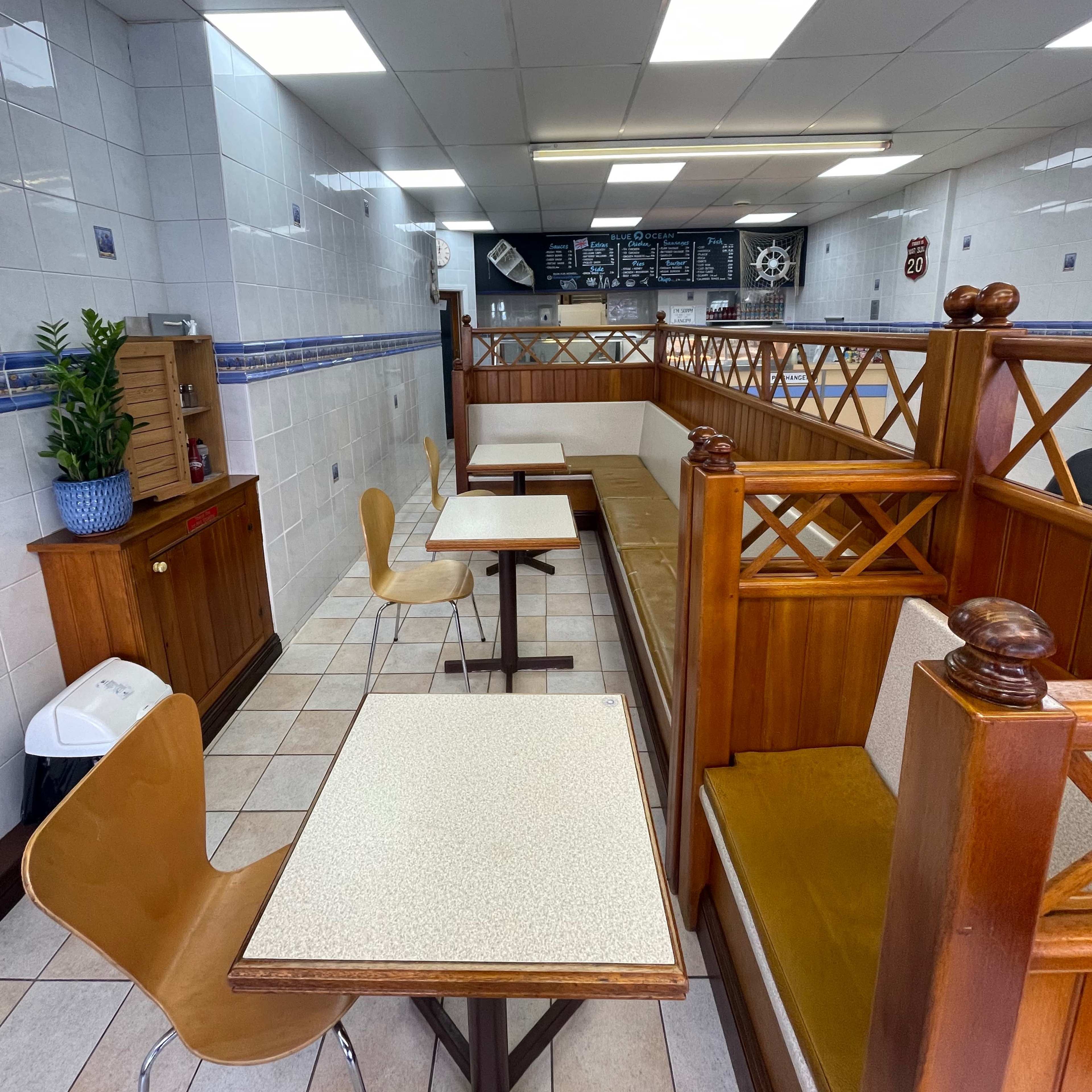 A small cafe interior with wooden seating, tables, and a counter displaying the menu in the background.