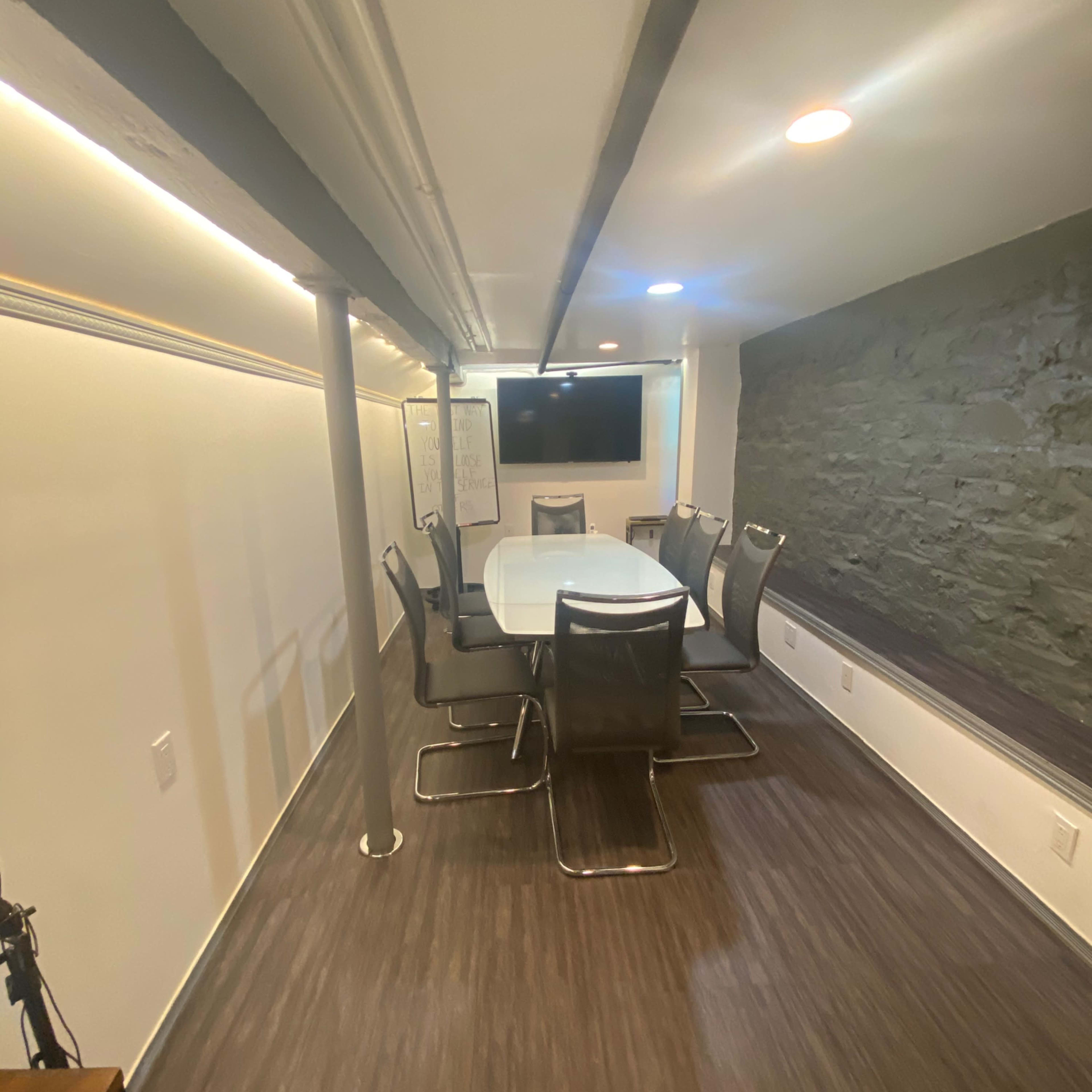 A modern conference room with a large white table, several chairs around it, and a wall-mounted television.