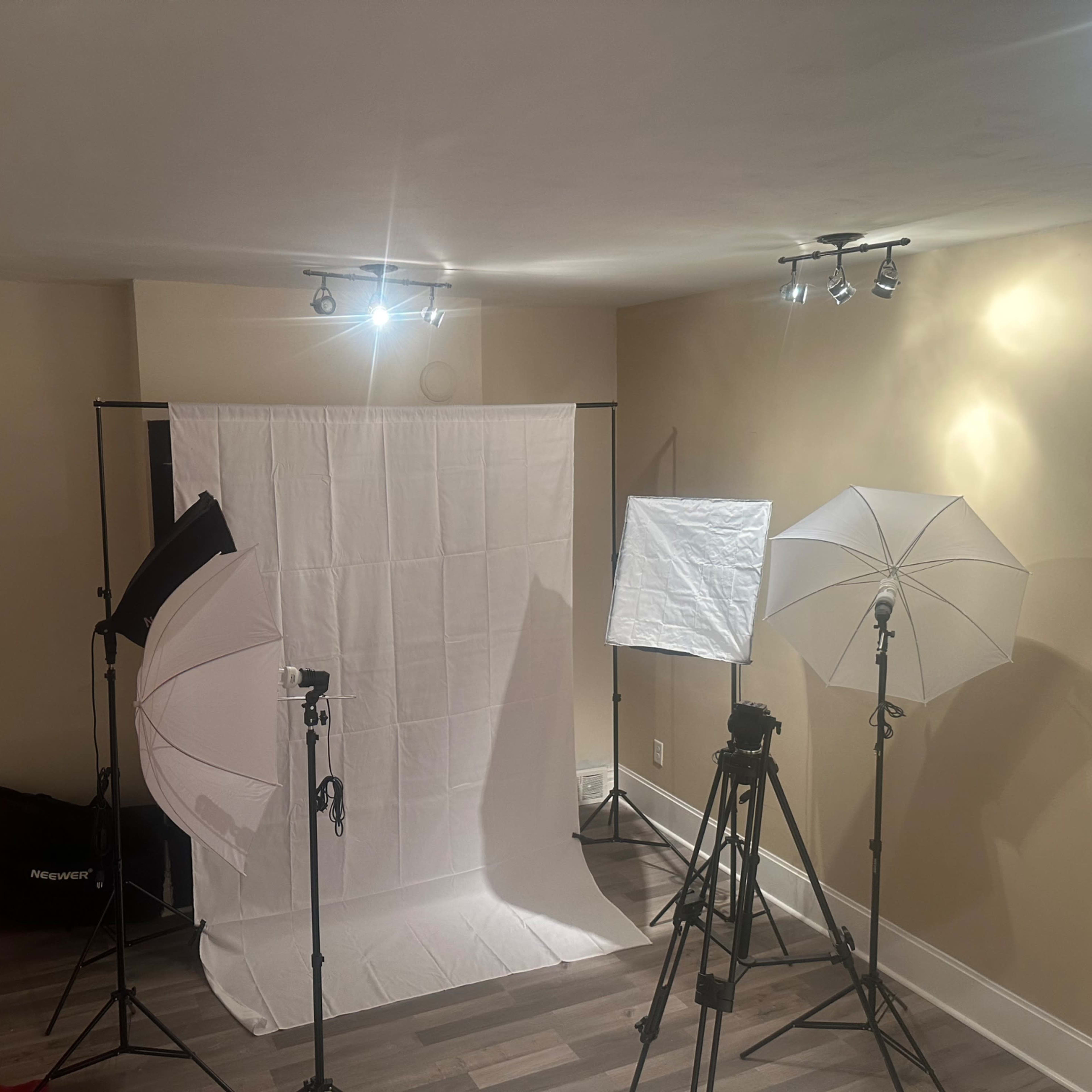 A photography setup with a white backdrop, two light tents, and three tripods positioned in a room with beige walls and red curtains.