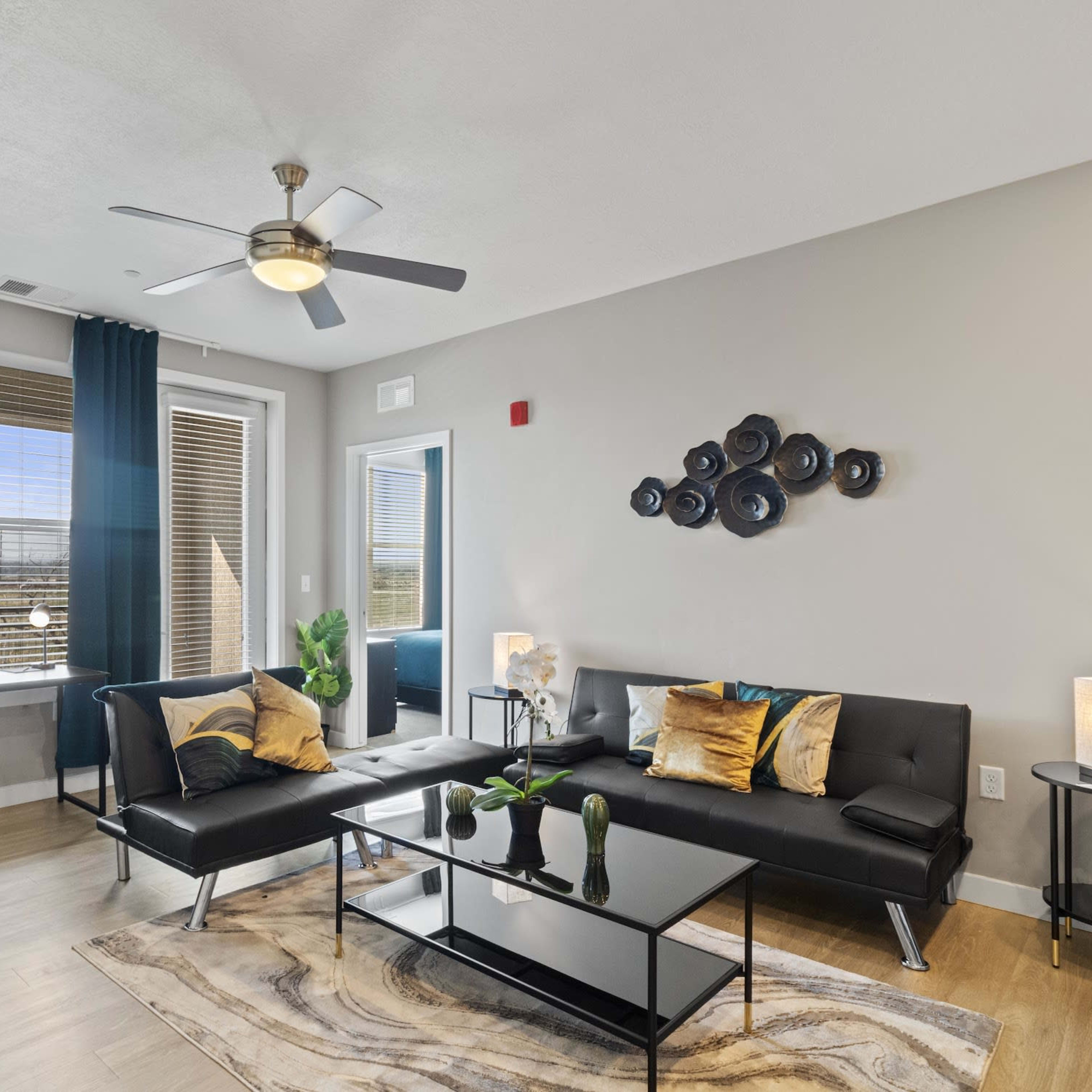 A modern living room with a black leather sectional sofa, a coffee table, and large windows dressed in dark curtains.