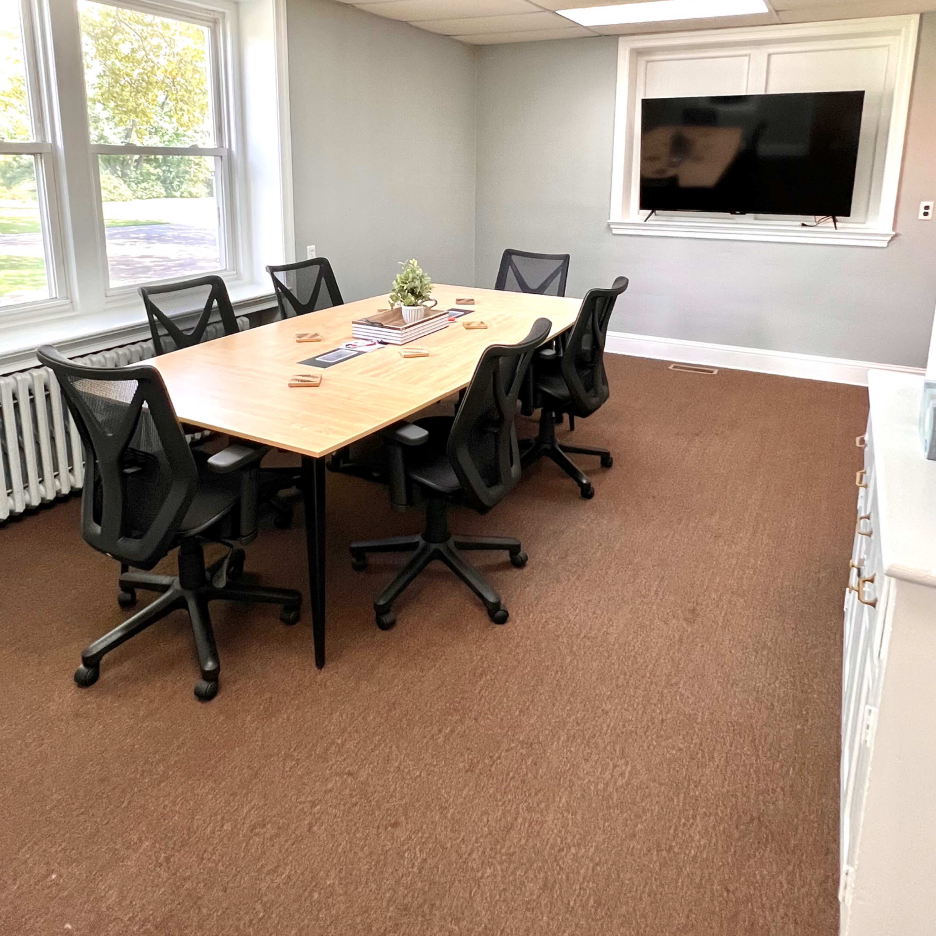 A meeting room with a rectangular table surrounded by six black office chairs and a mounted television on the wall.