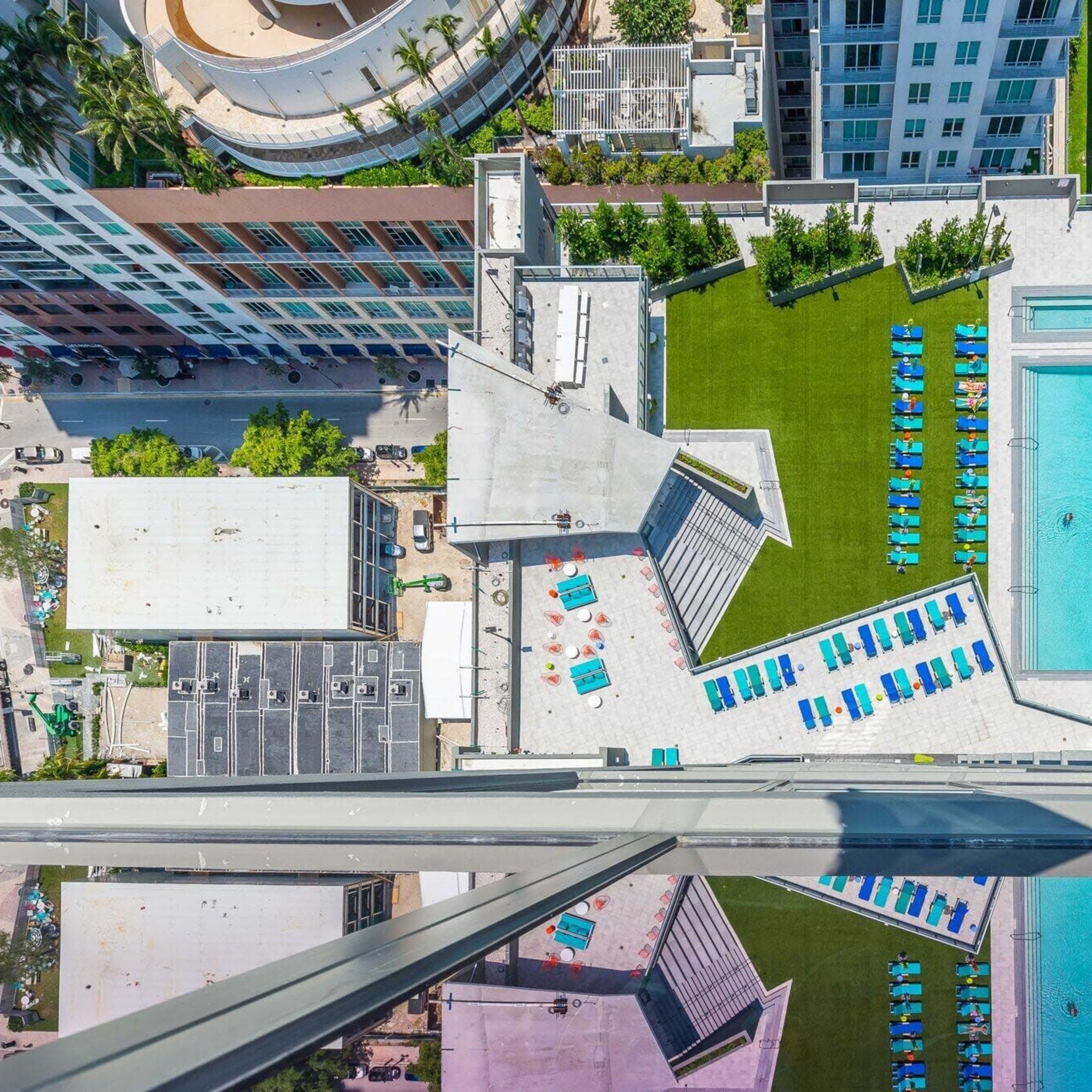 A rooftop pool area surrounded by lounge chairs, grassy space, and nearby buildings in an urban setting.