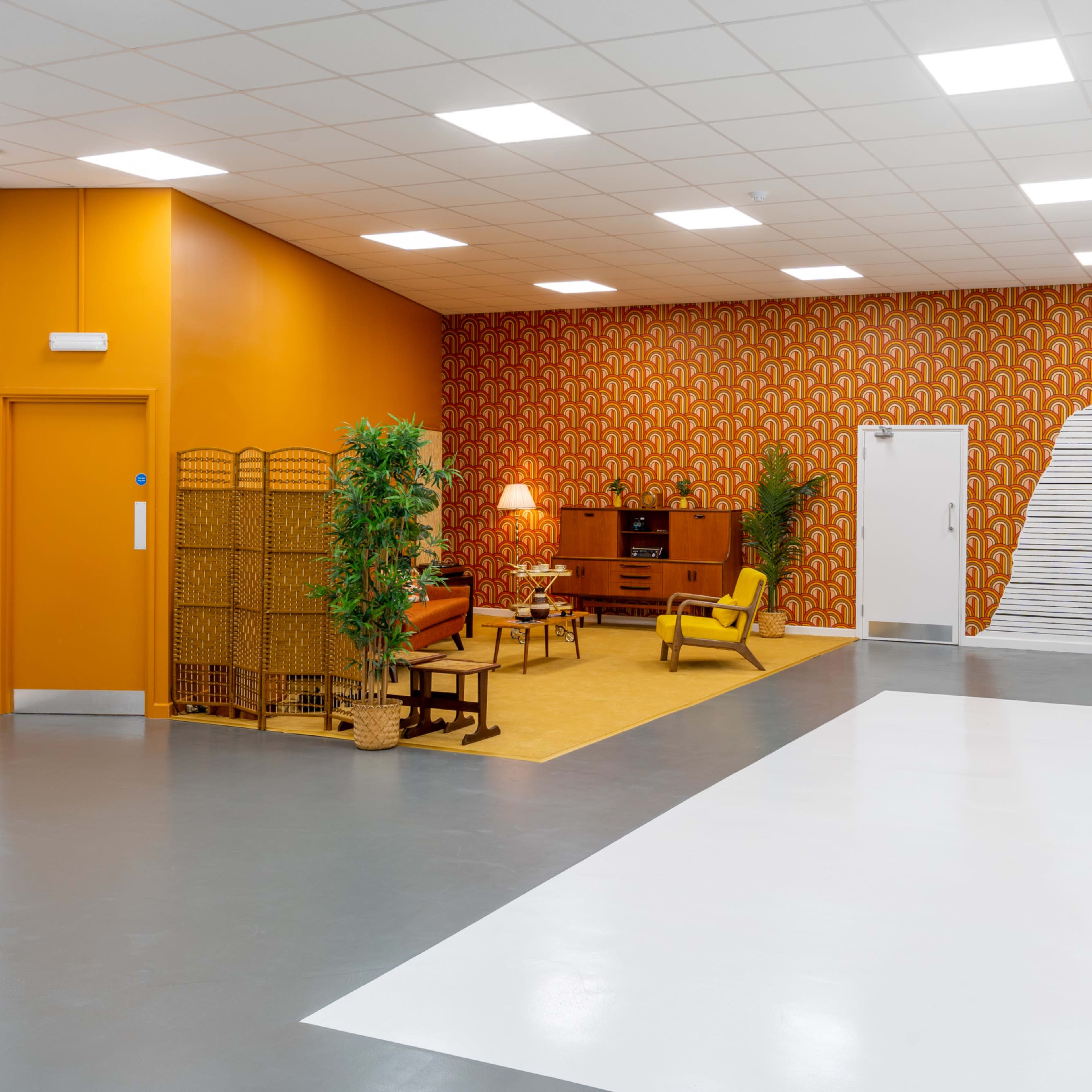 A spacious room with a retro-themed sitting area featuring an orange accent wall, patterned wallpaper, and yellow furniture.