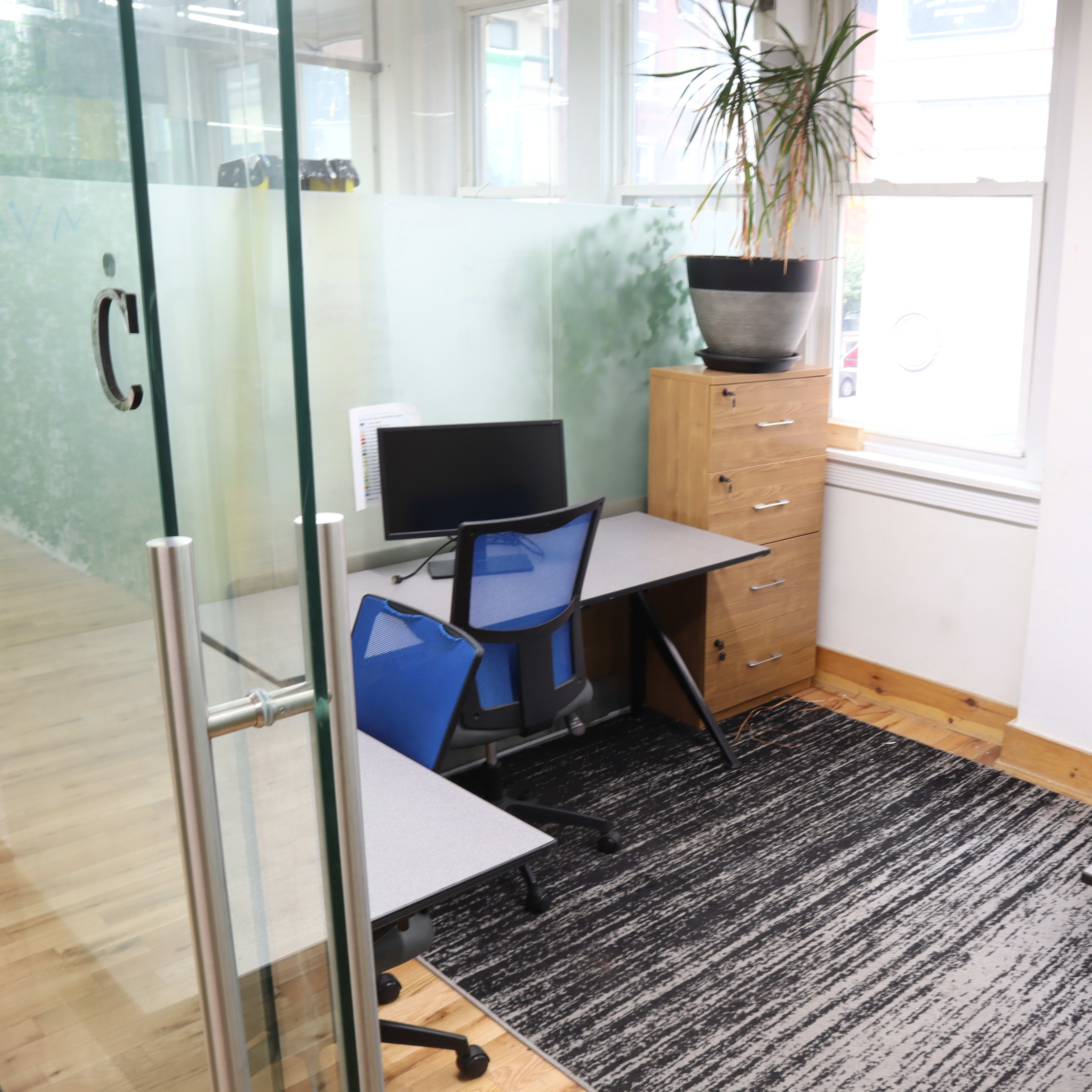 A modern office space with two desks, a computer, and a plant beside a large window.