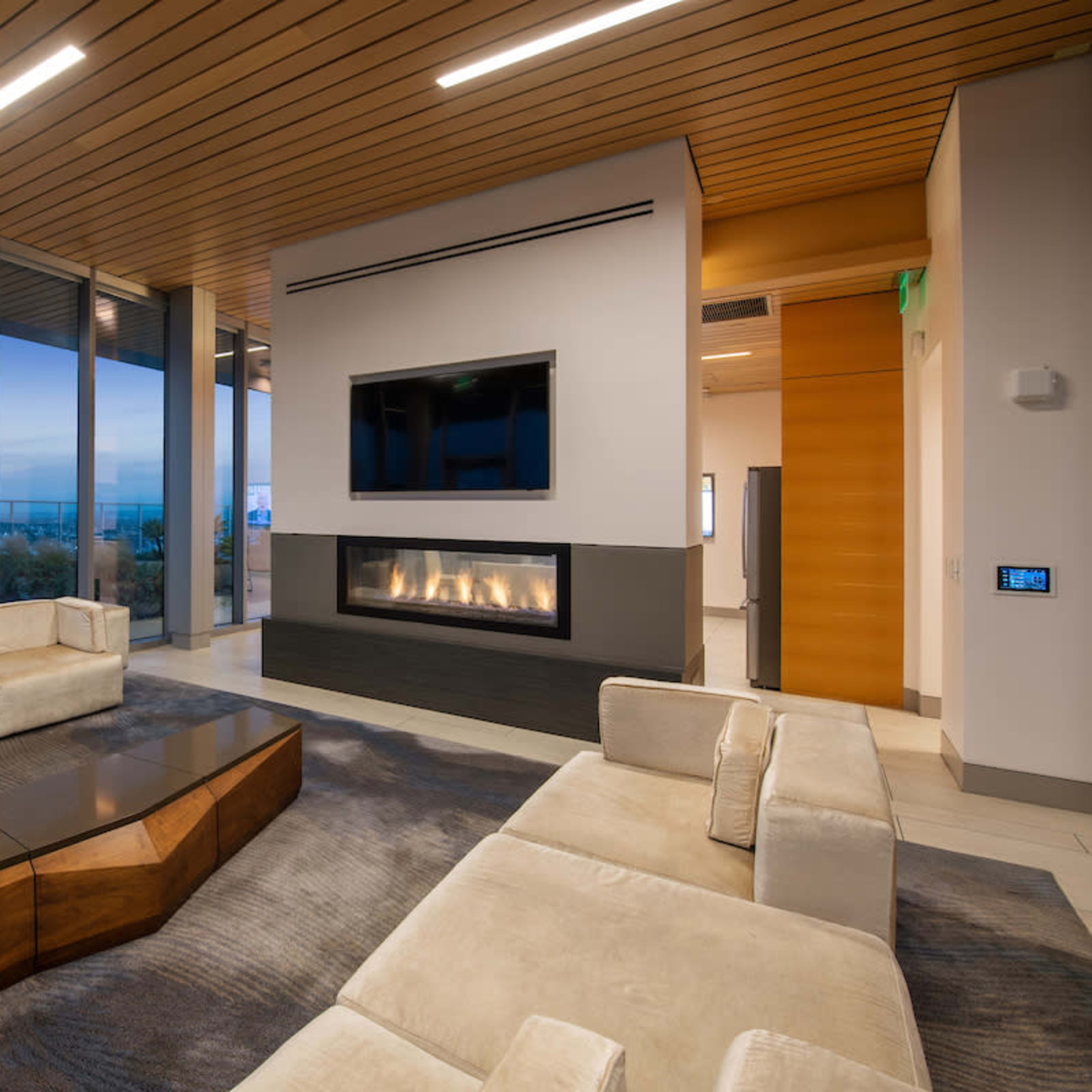 A modern living room features large windows, a minimalist fireplace, and comfortable seating arranged around a coffee table.