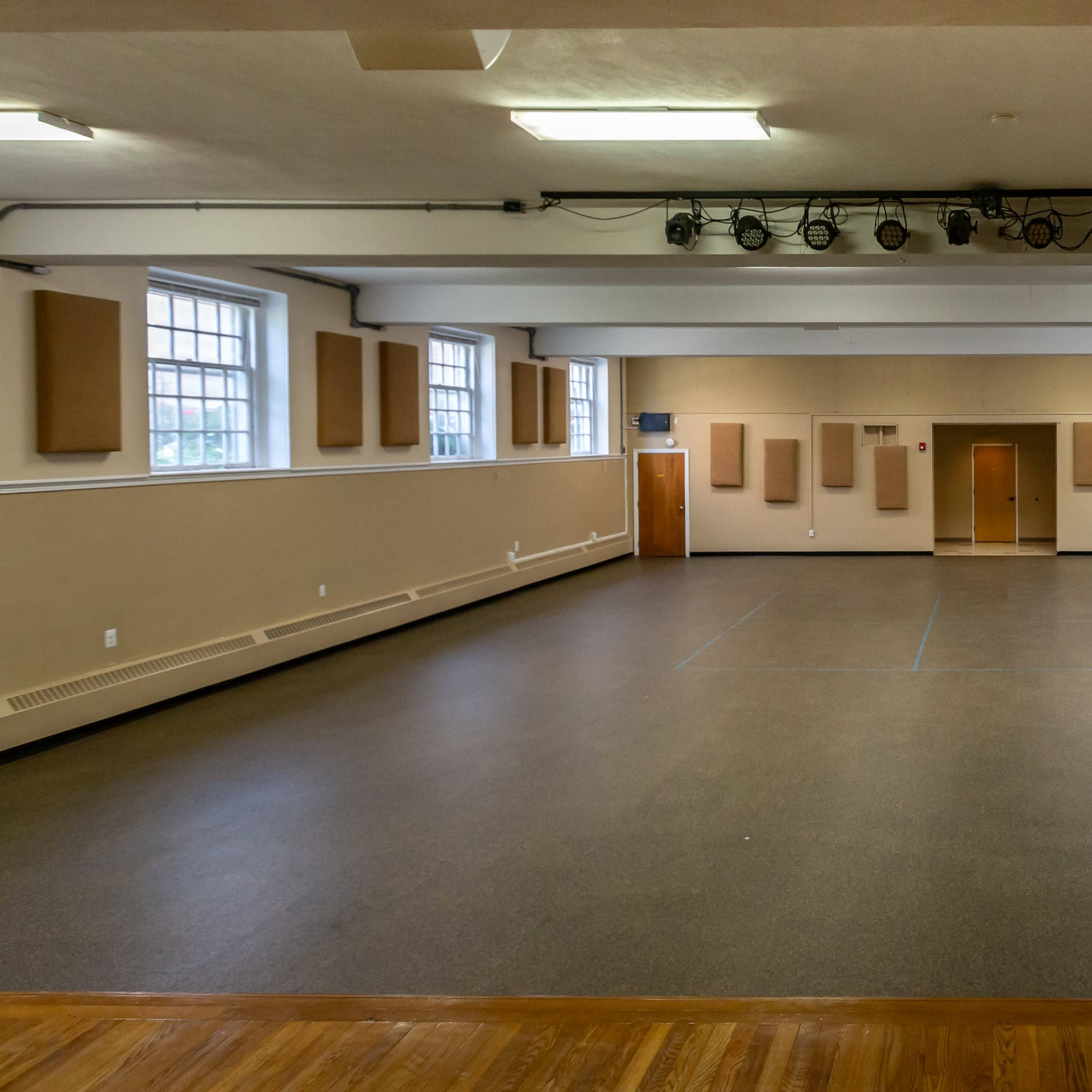 A spacious indoor hall with a polished wooden floor, beige walls, and sound-absorbing panels placed along the sides.