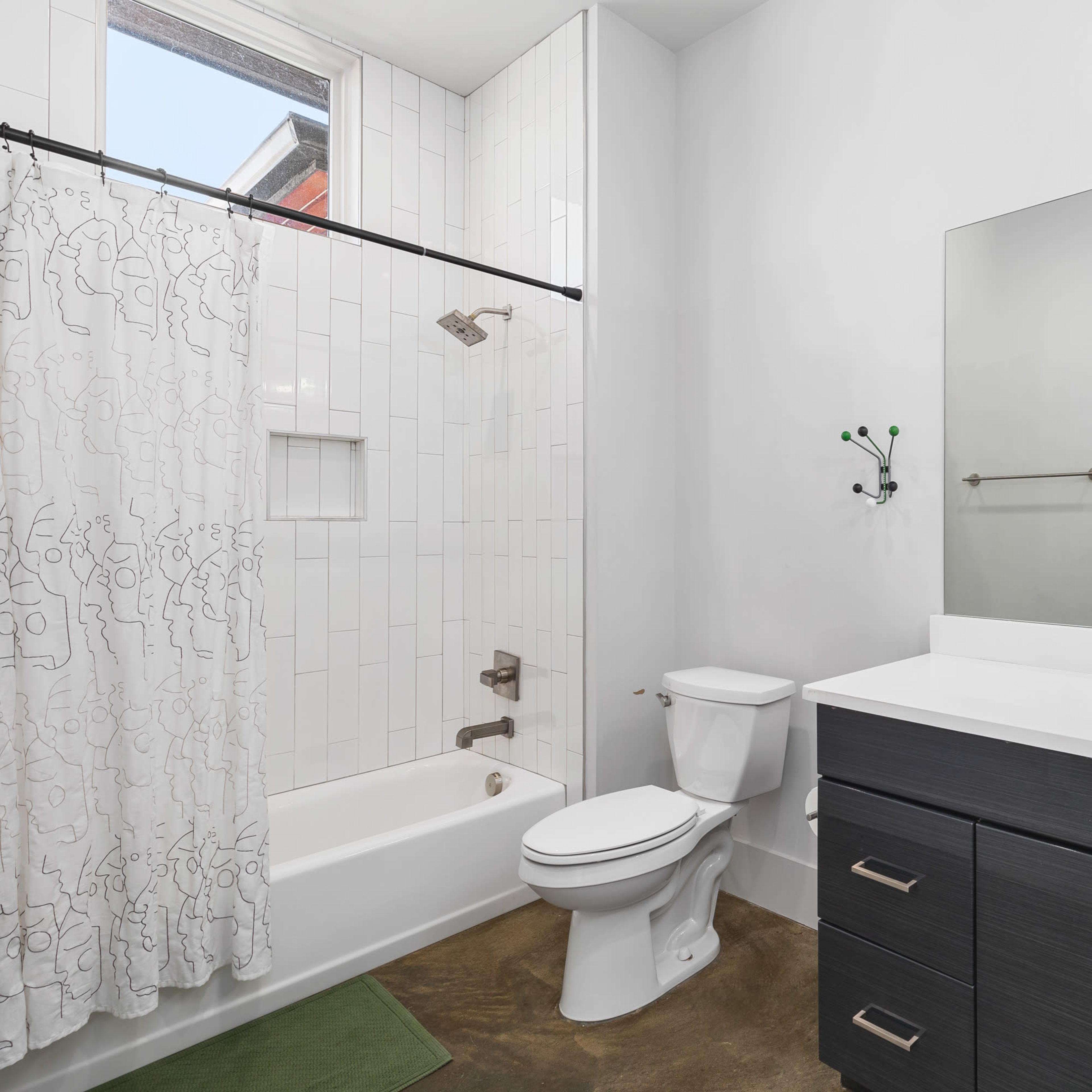 A modern bathroom featuring a bathtub with tile surround, a toilet, a double sink vanity with dark cabinetry, and a large mirror.