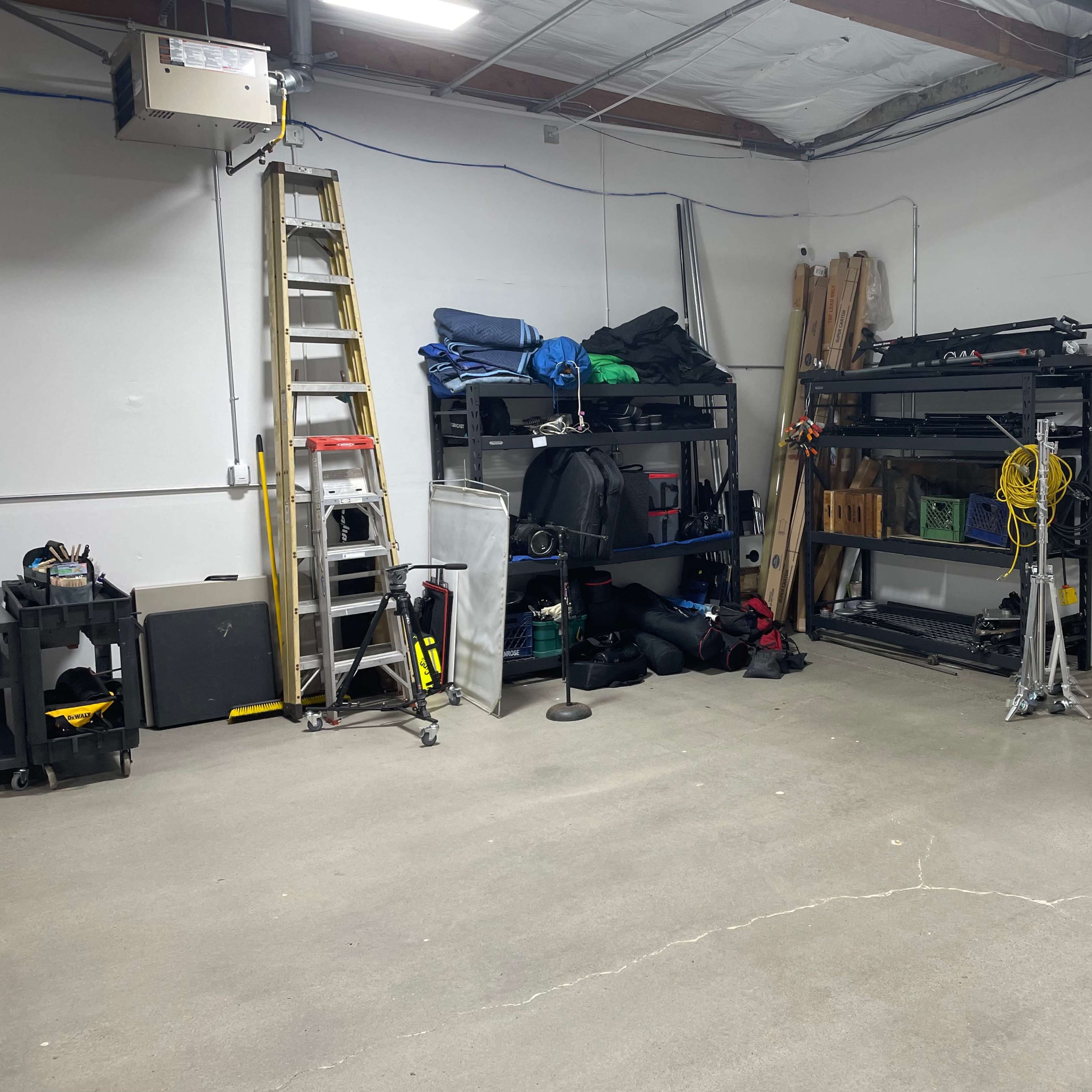 A garage interior with shelving units filled with various tools and equipment, a ladder, and a partially open door.