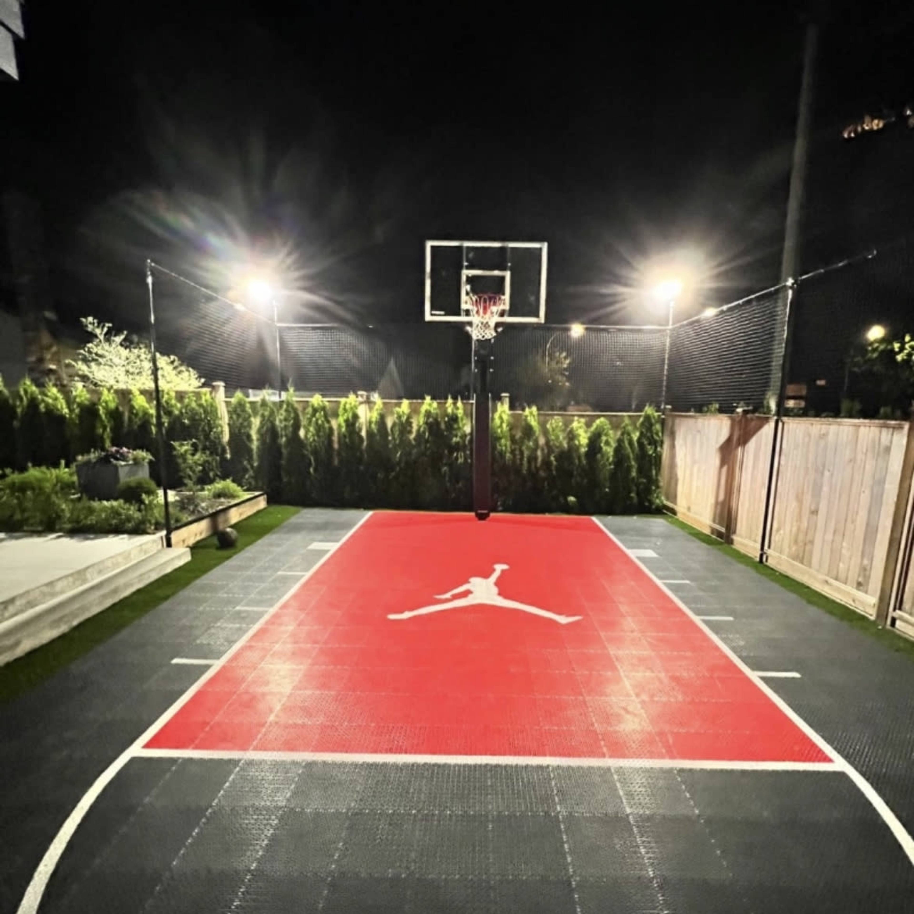 A brightly lit basketball court with a red surface featuring a large Jumpman logo and a hoop at one end.