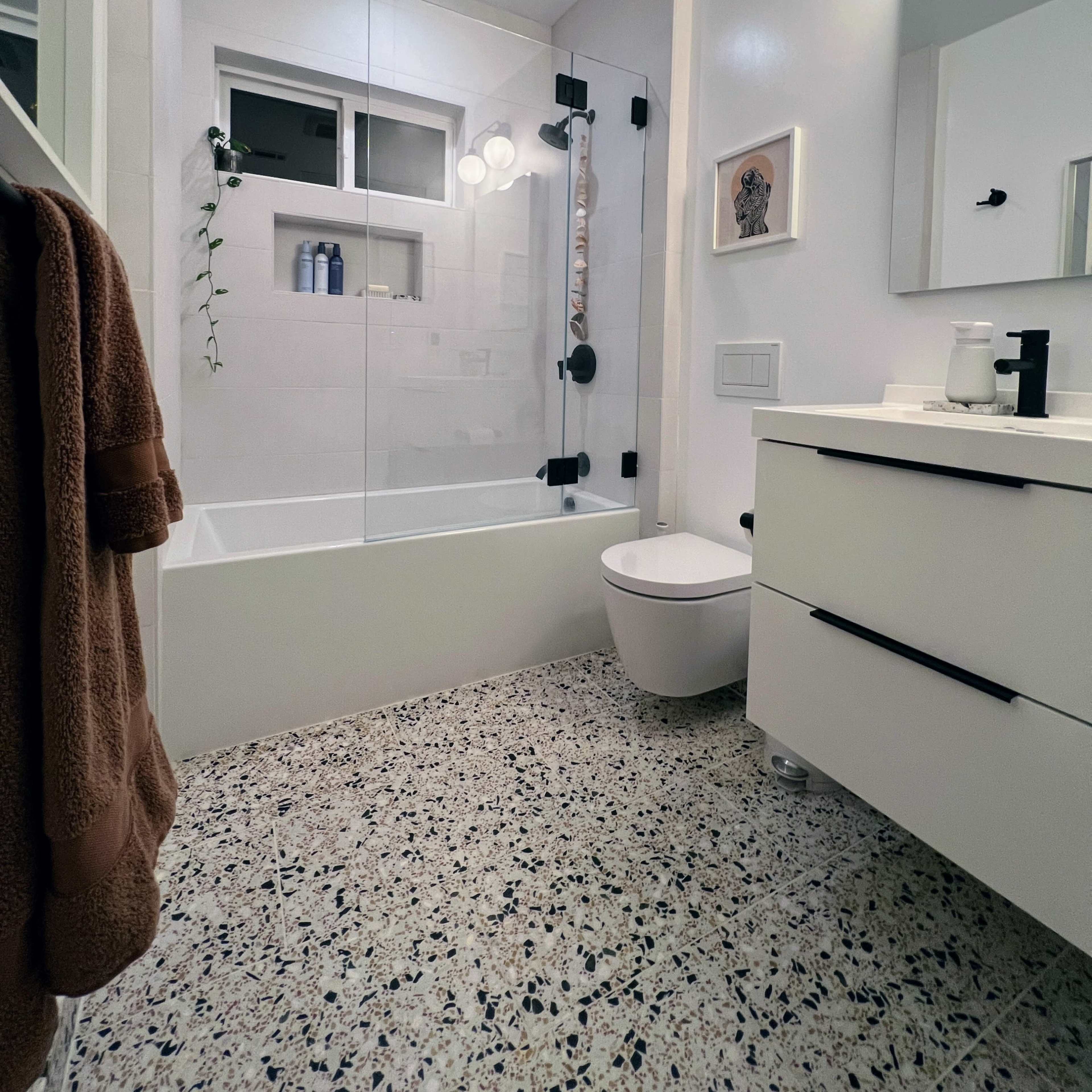 The bathroom features a glass shower enclosure, a modern white vanity, and a terrazzo floor.