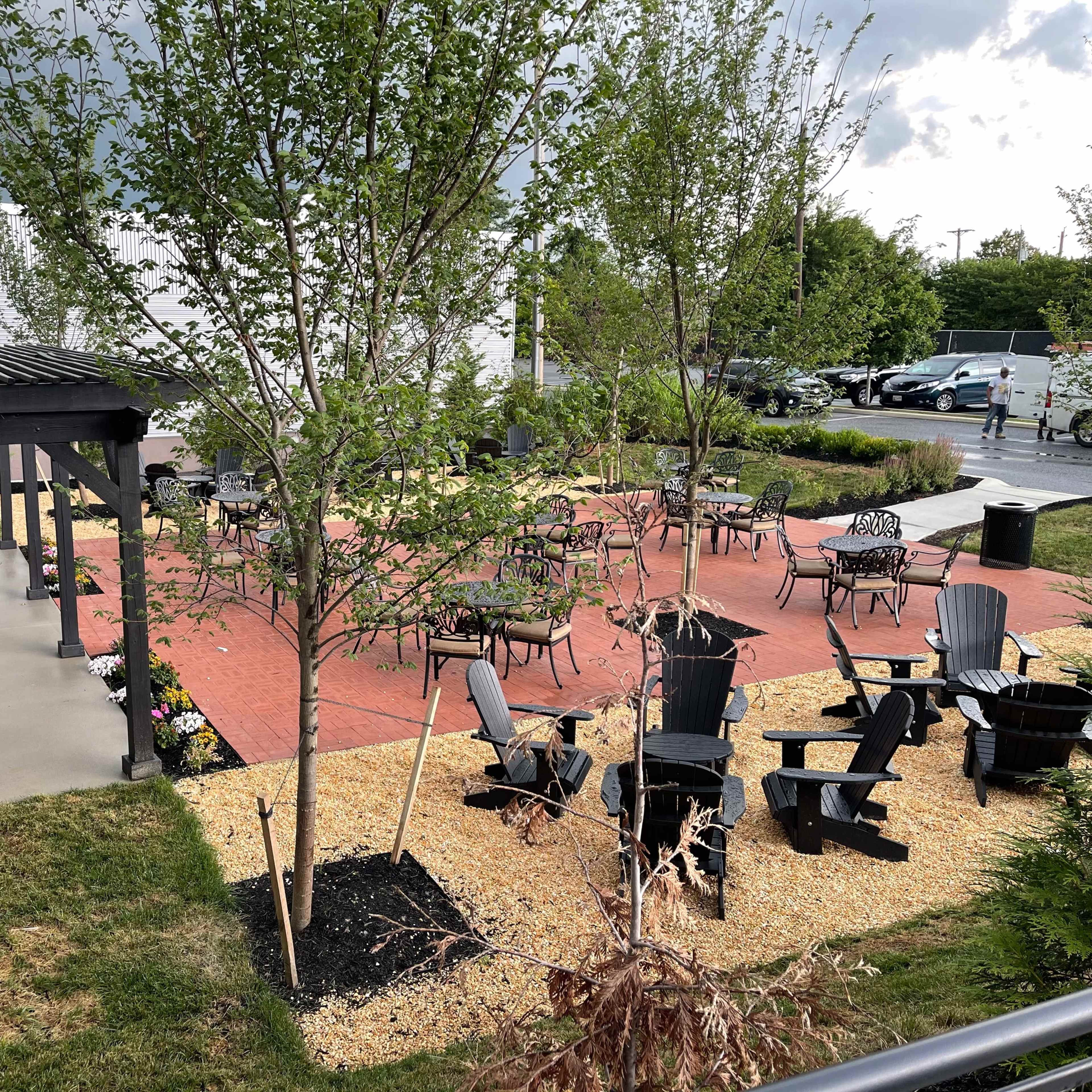 A landscaped outdoor patio area with seating arrangements, including black chairs and tables, surrounded by gravel and trees.