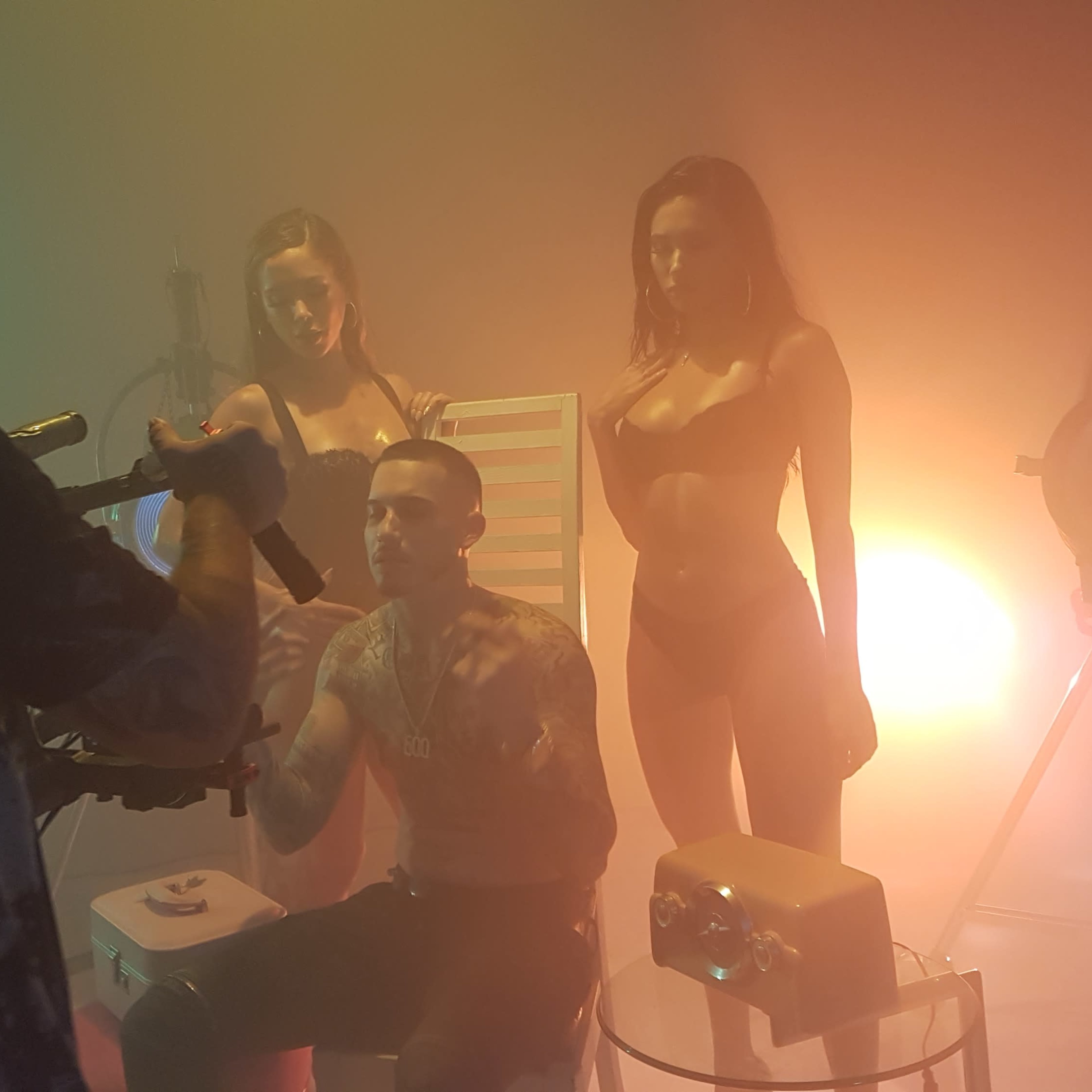 A photographer captures a model posing with two women in a studio illuminated by colorful lights and fog.