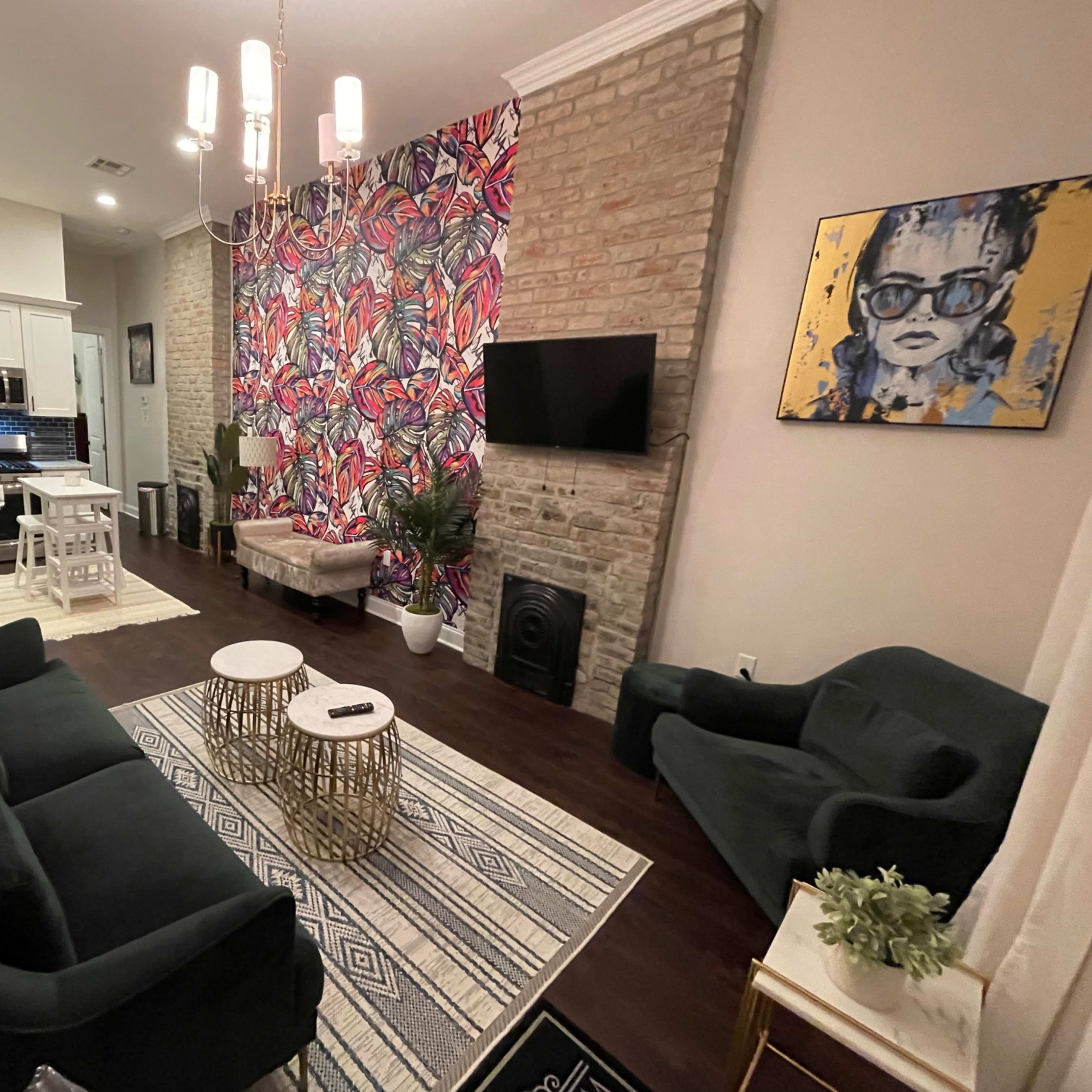 A modern living area with dark green sofas, a patterned accent wall, a television, and a mix of decorative elements like plants and a coffee table.