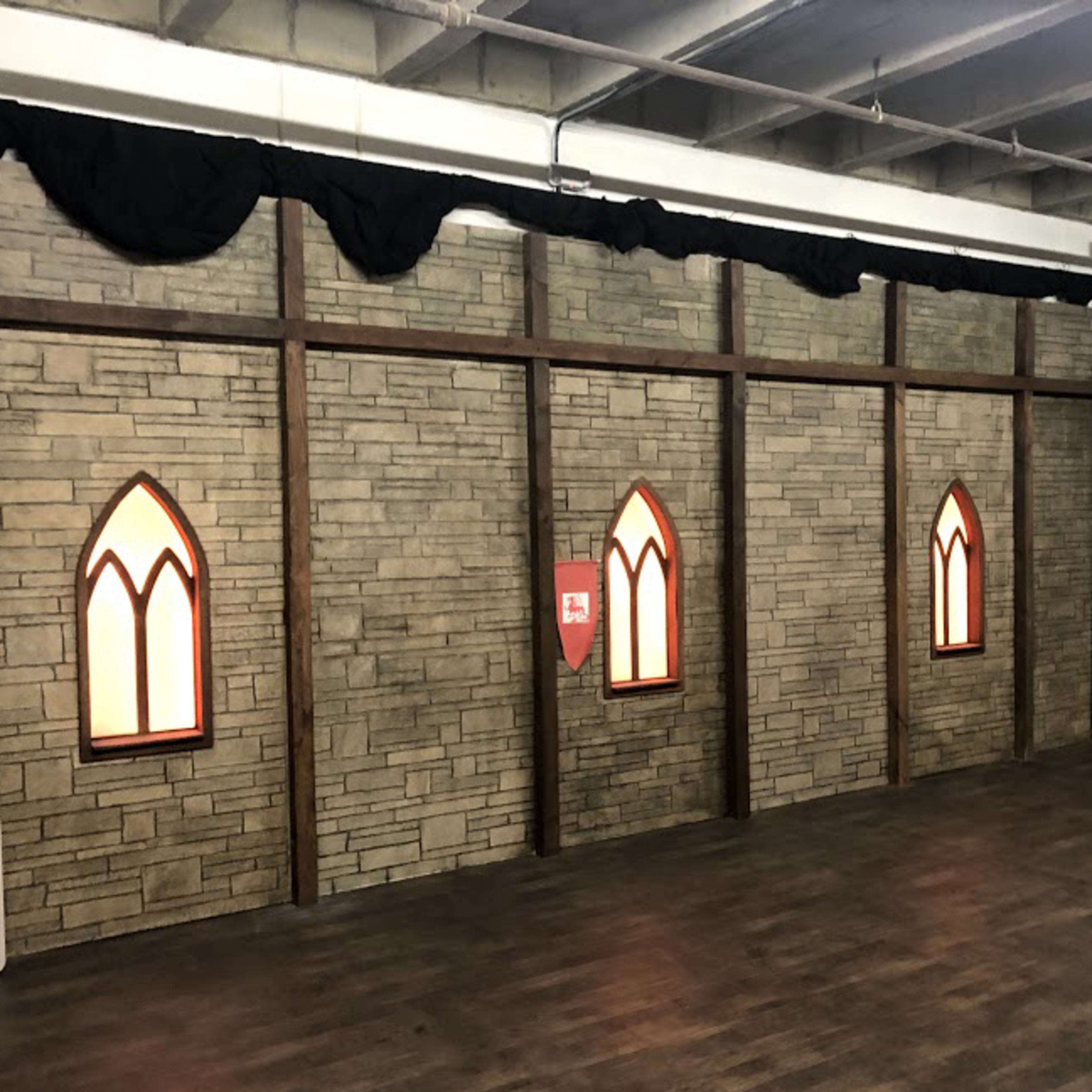 An interior room with stone-patterned walls, decorative windows resembling stained glass, and wooden beams.