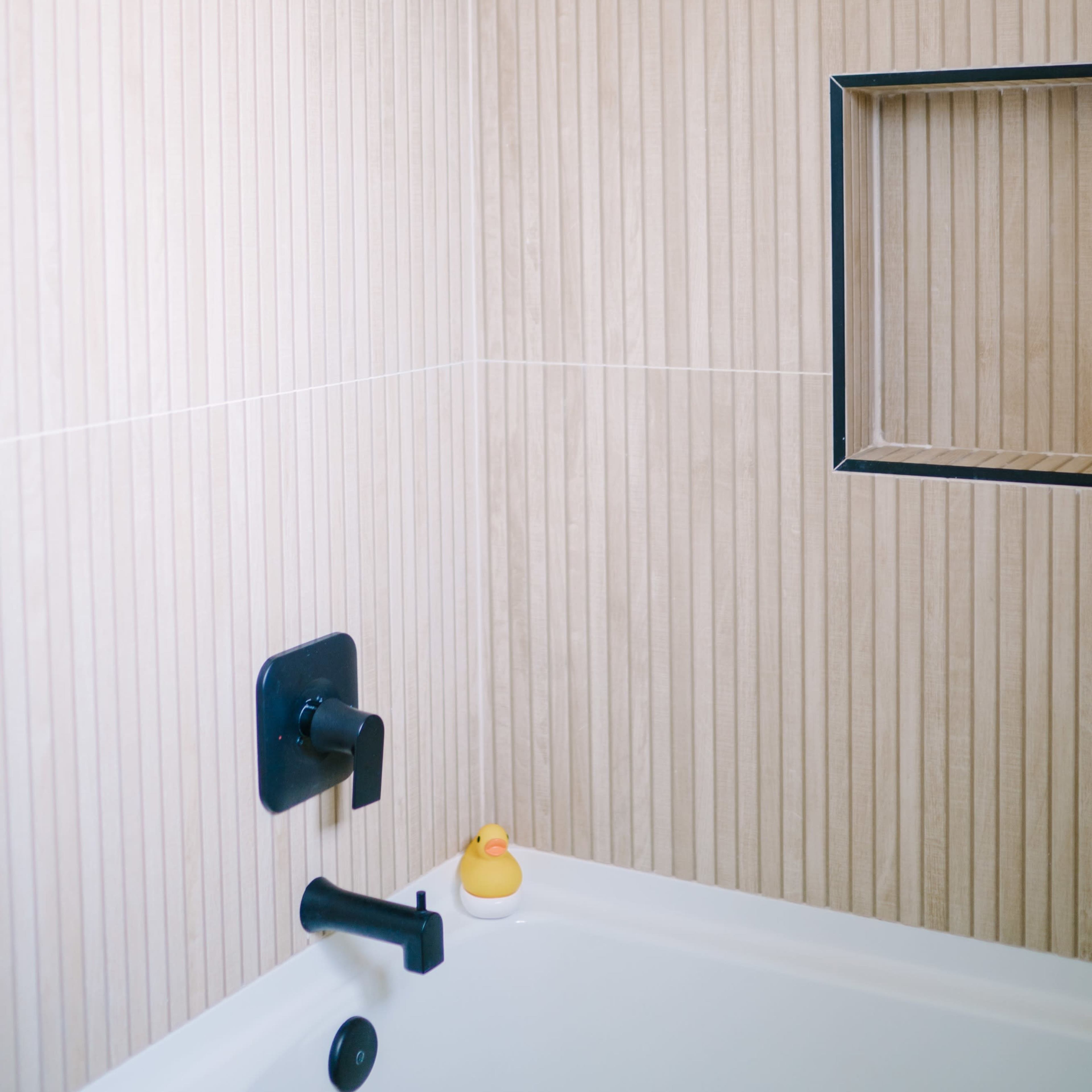 A corner of a shower with vertical wooden-patterned walls, a showerhead, a black faucet, and a small cubby containing a rubber duck.
