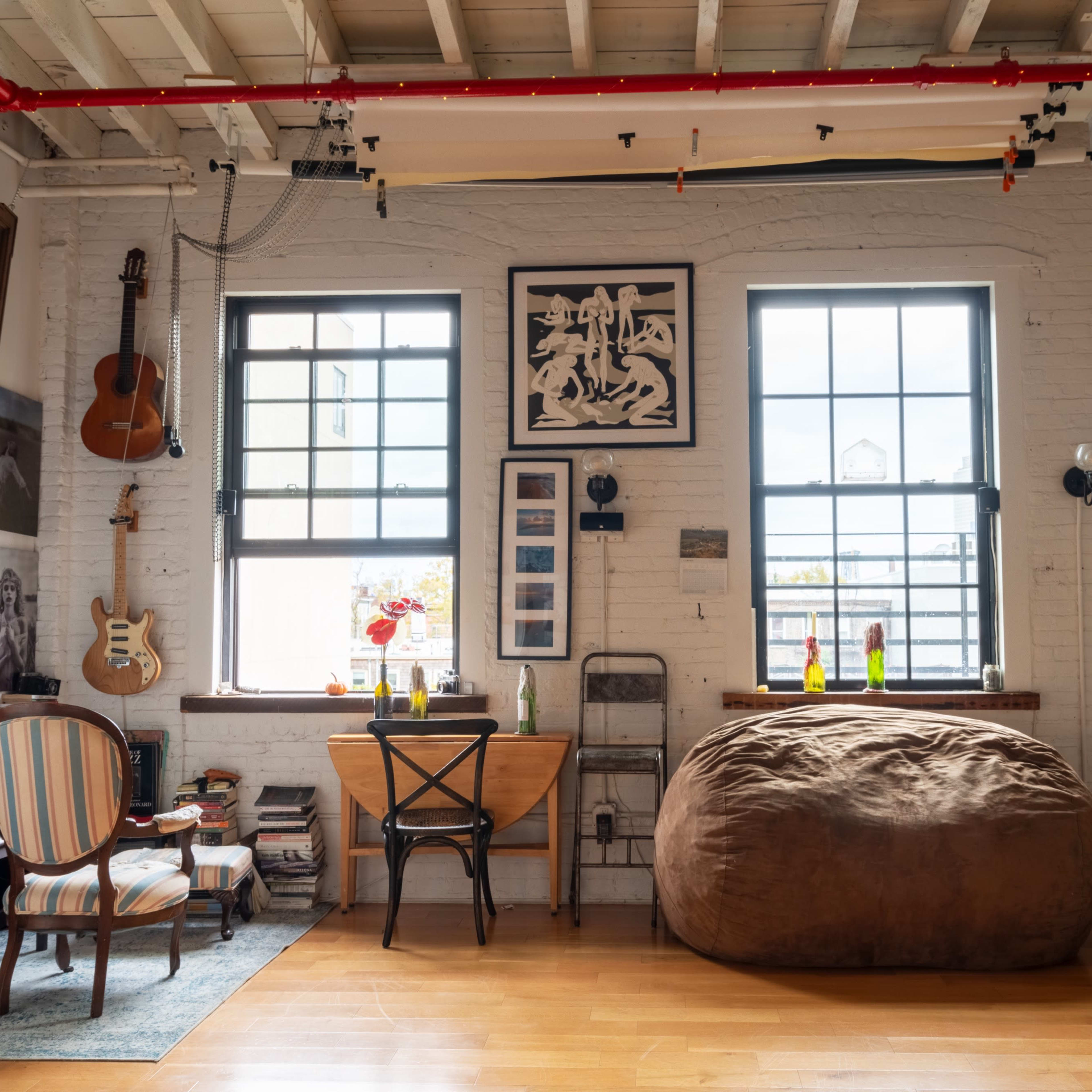 A cozy room with large windows, a piano, a table with chairs, a bean bag, and various art pieces on the walls.