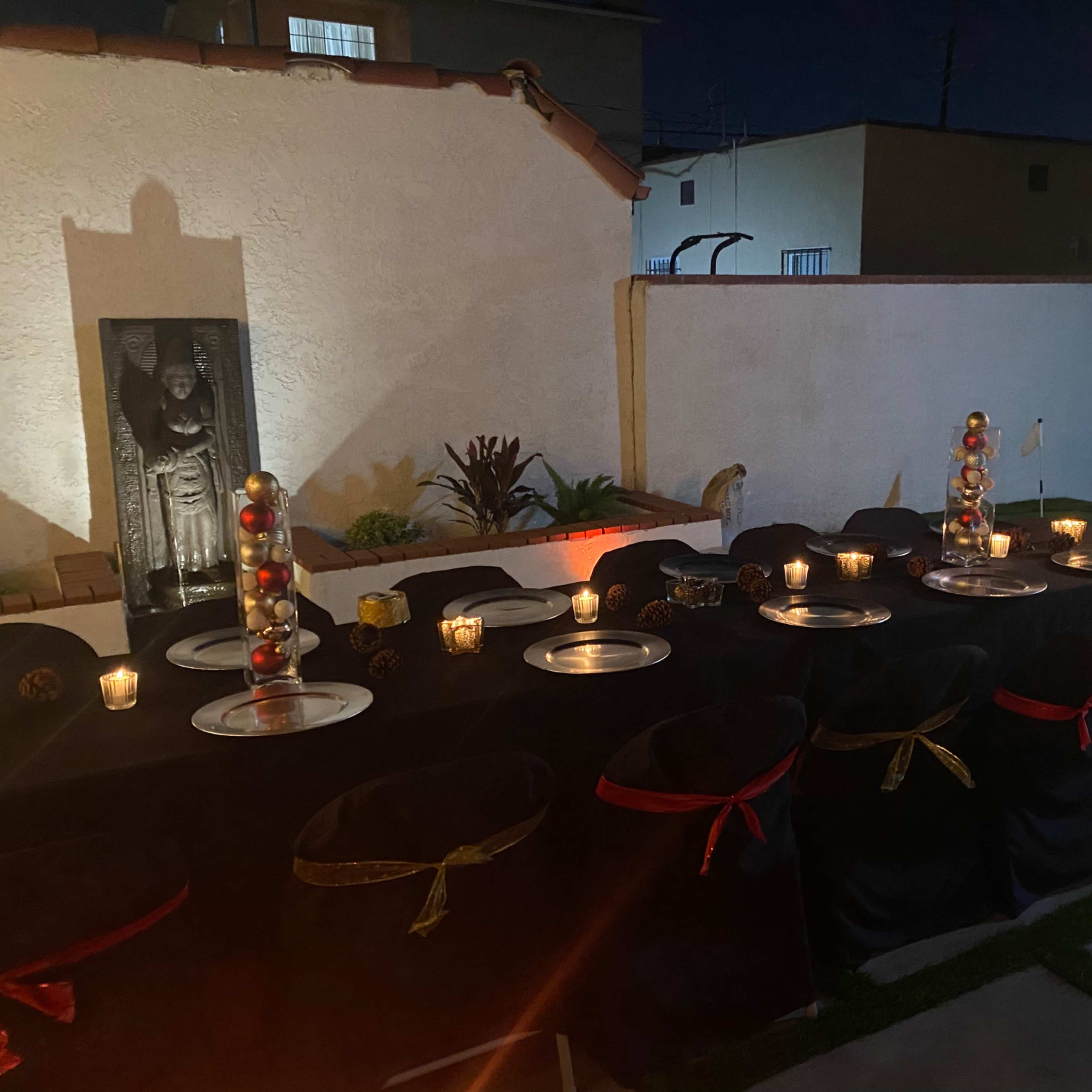 A long table is set for dining in an outdoor space, illuminated by candles and surrounded by decorative elements.