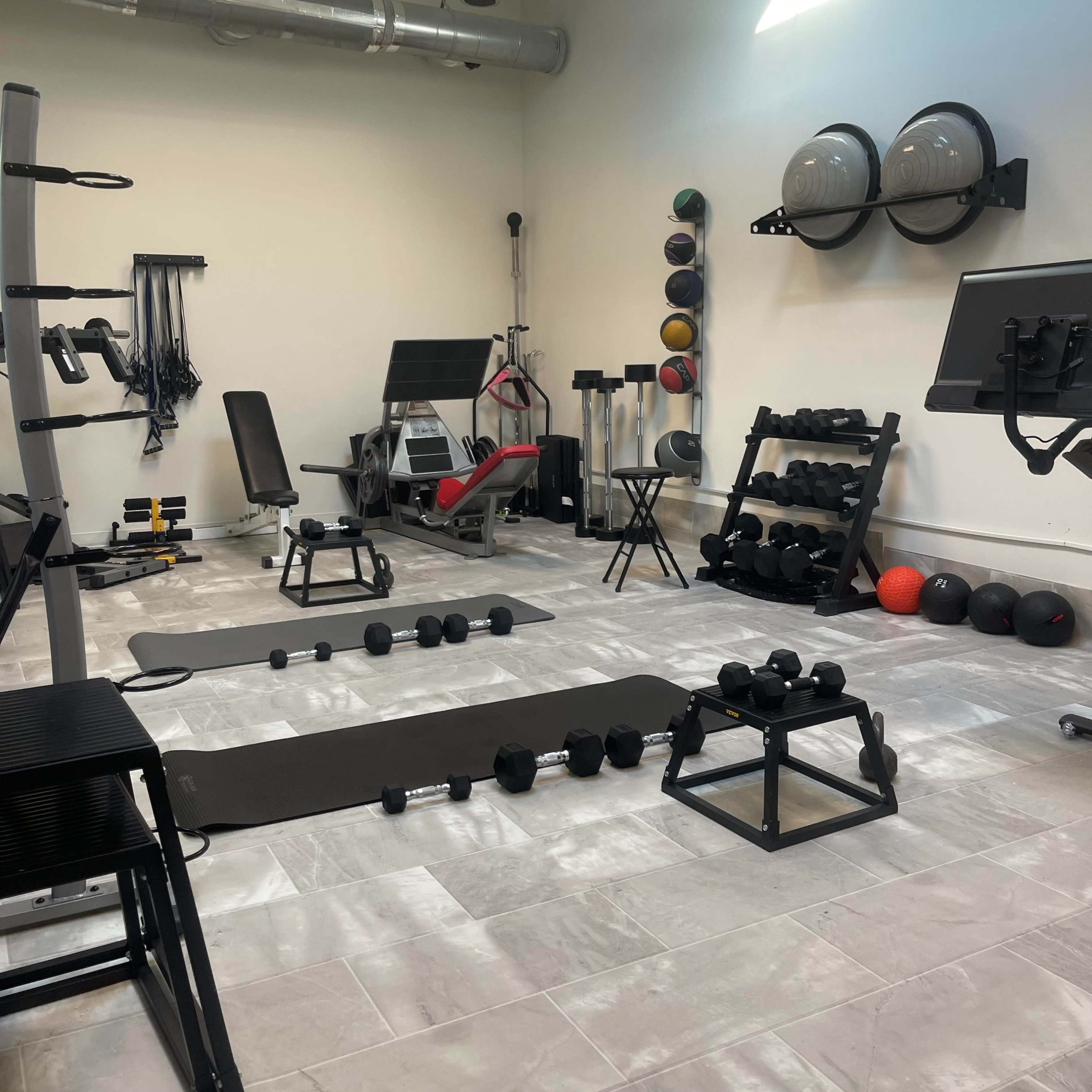 A well-equipped gym with various weights, exercise machines, and workout mats arranged in a spacious area.