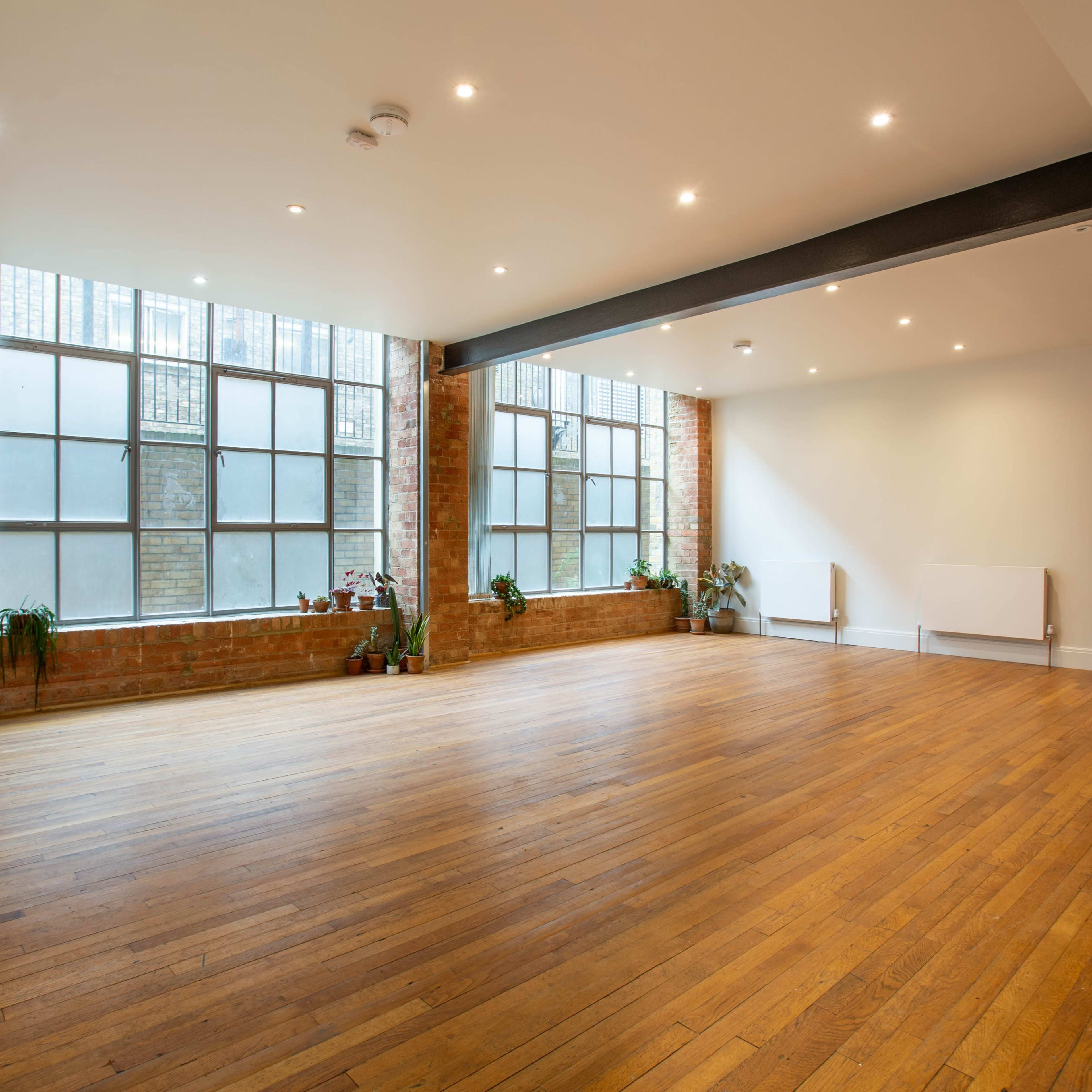 A spacious room with large windows, brick walls, and wooden flooring.