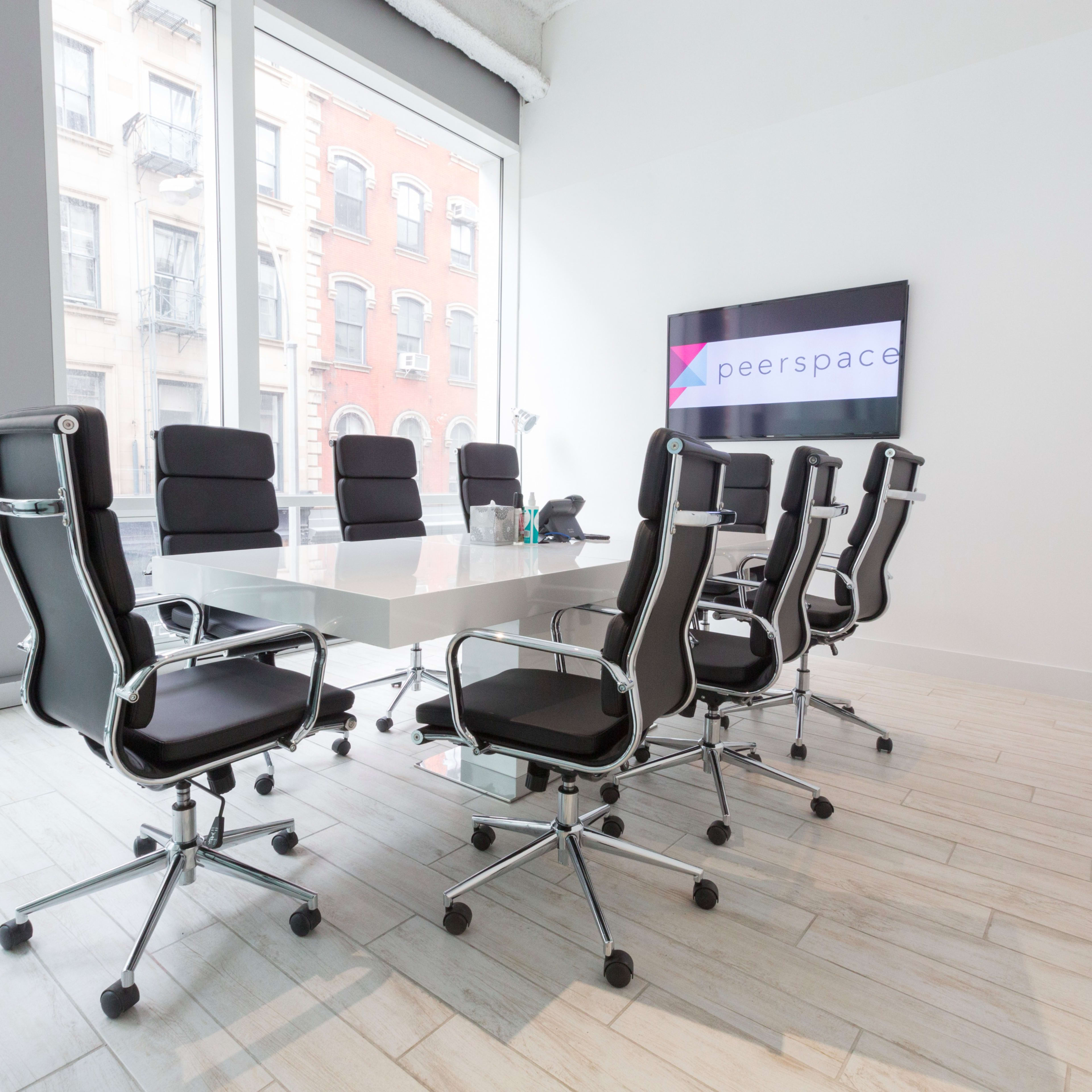 A modern conference room features a large white table surrounded by black swivel chairs, with a television displaying the Peerspace logo on the wall.