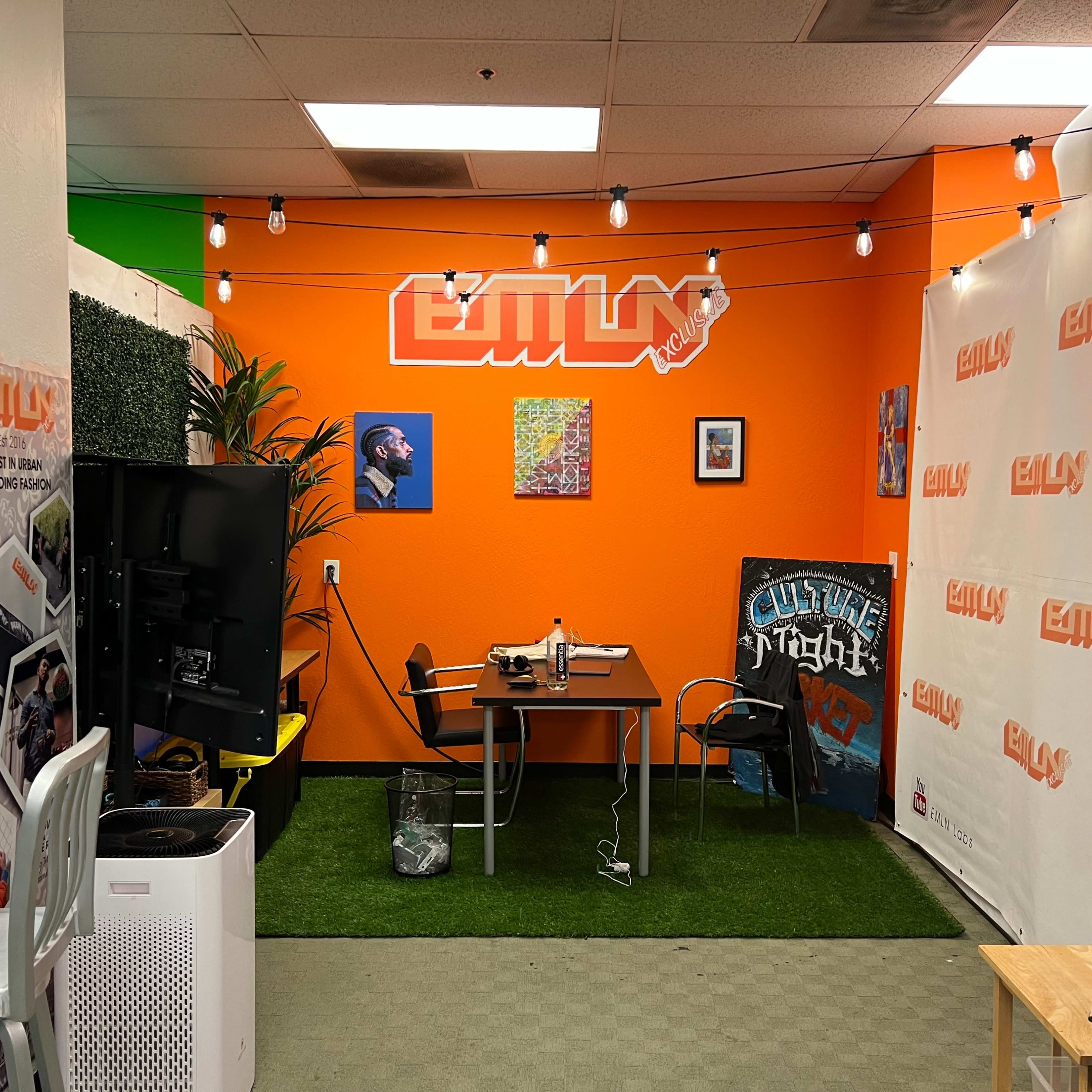 A small office space with an orange wall, a desk, a television, and decorative elements including plants and string lights.