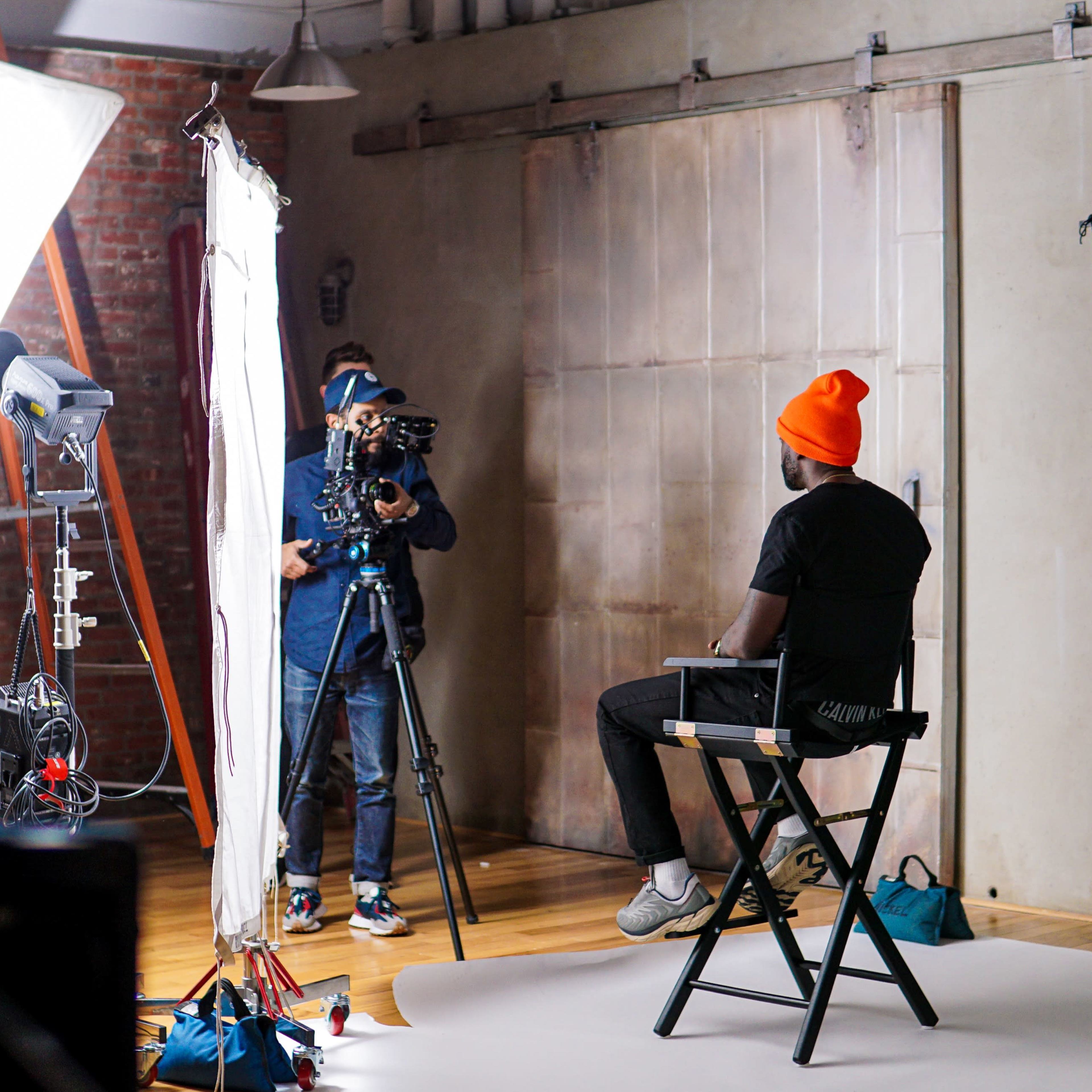 A spacious photography studio with a large white backdrop, wooden floors, and a modern design featuring a lofted area with seating and multiple entrances.