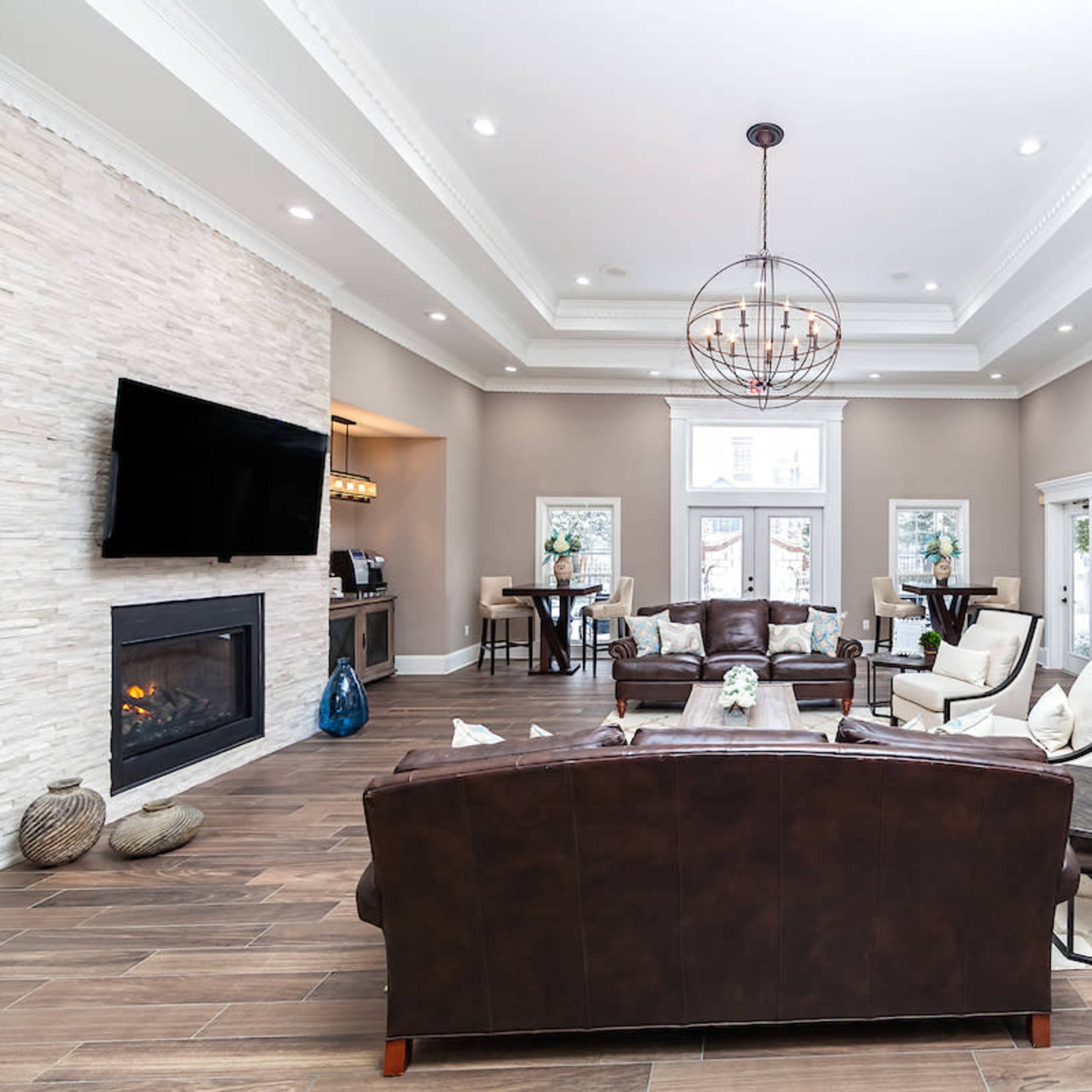 A spacious, modern living area with a dark leather sofa, a stone fireplace, and a kitchen visible in the background.