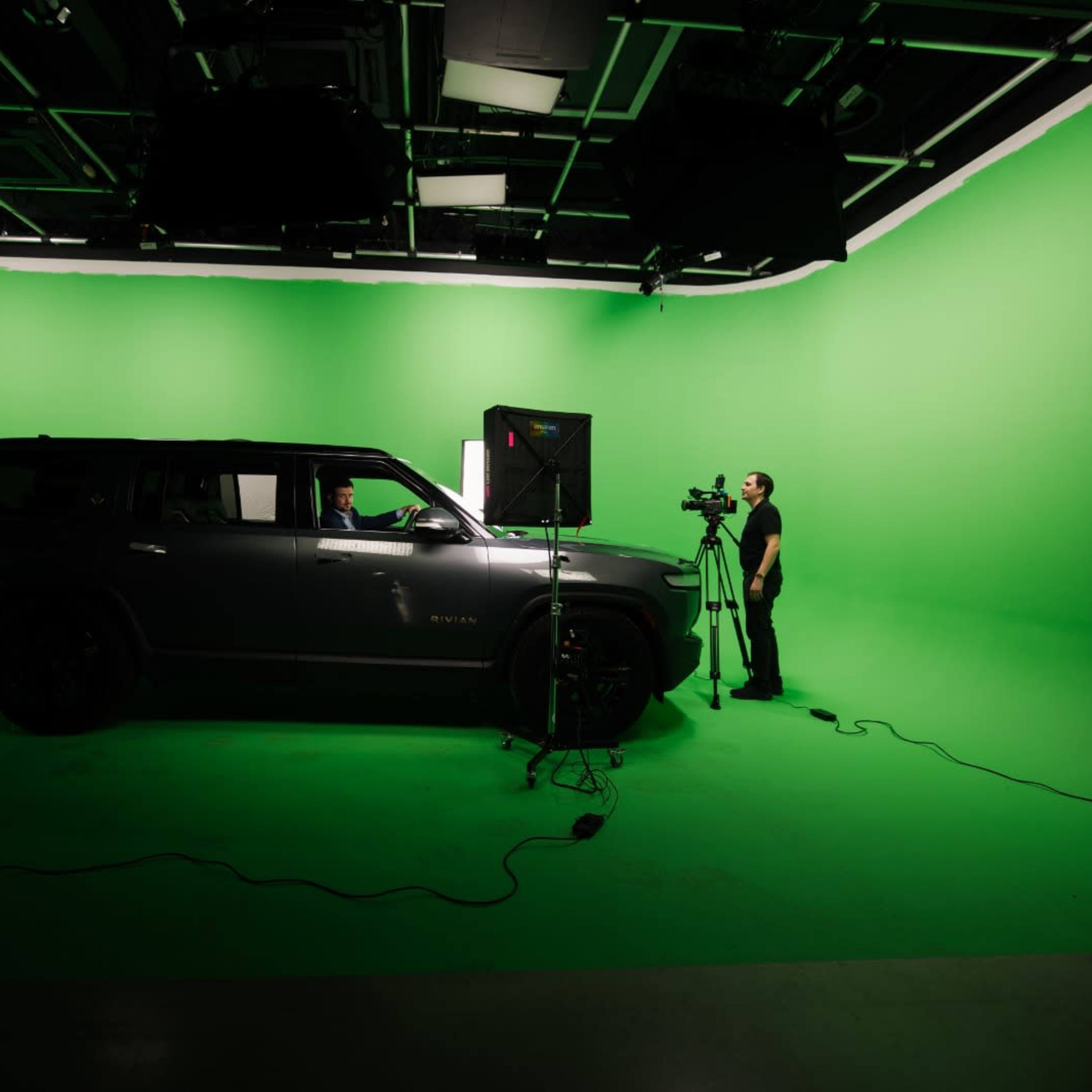 A gray SUV is positioned in a studio with a green backdrop, while a person operates a camera nearby.