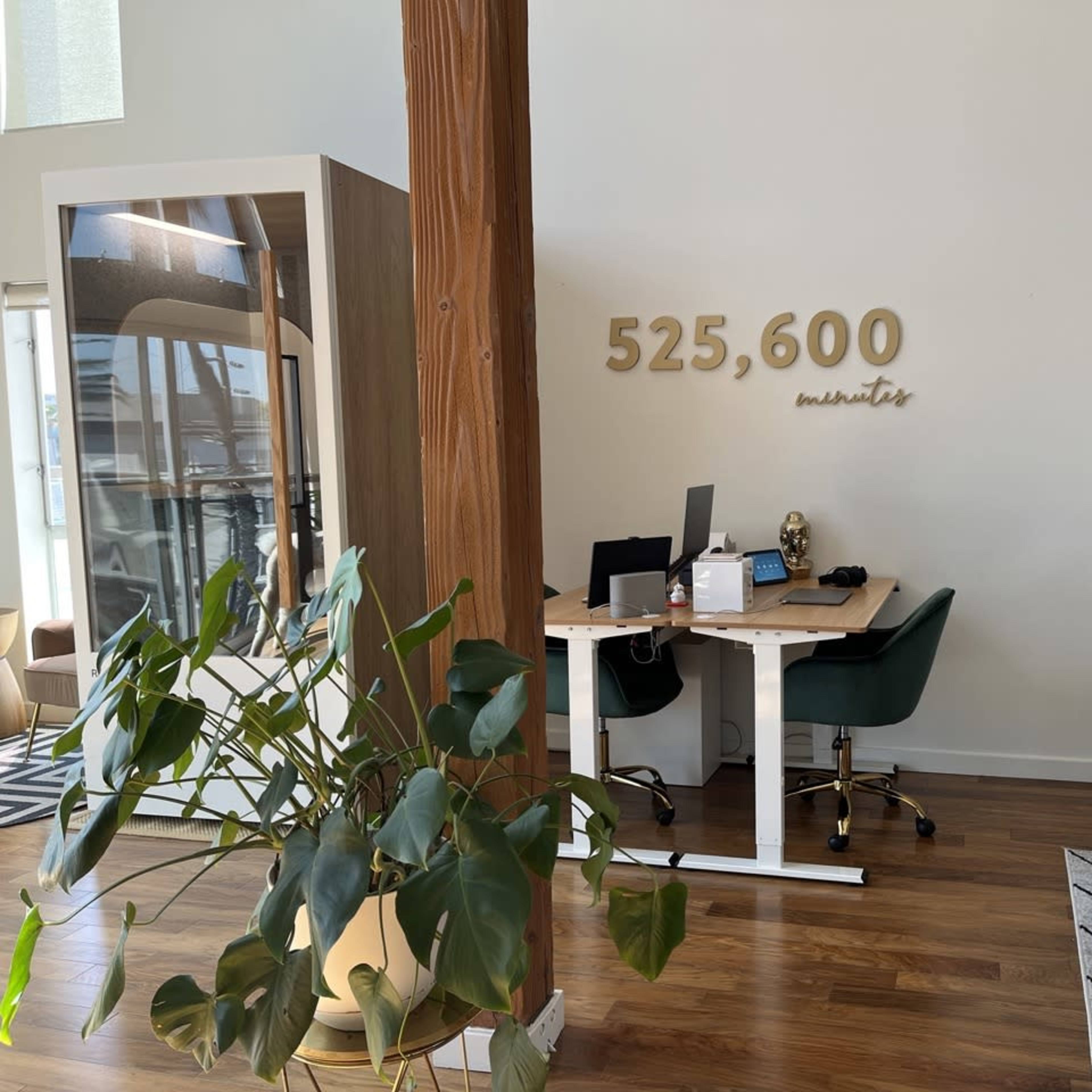 A modern office space features a desk with a computer, surrounded by plants, a pool table, and a large wall display reading "525,600 minutes."