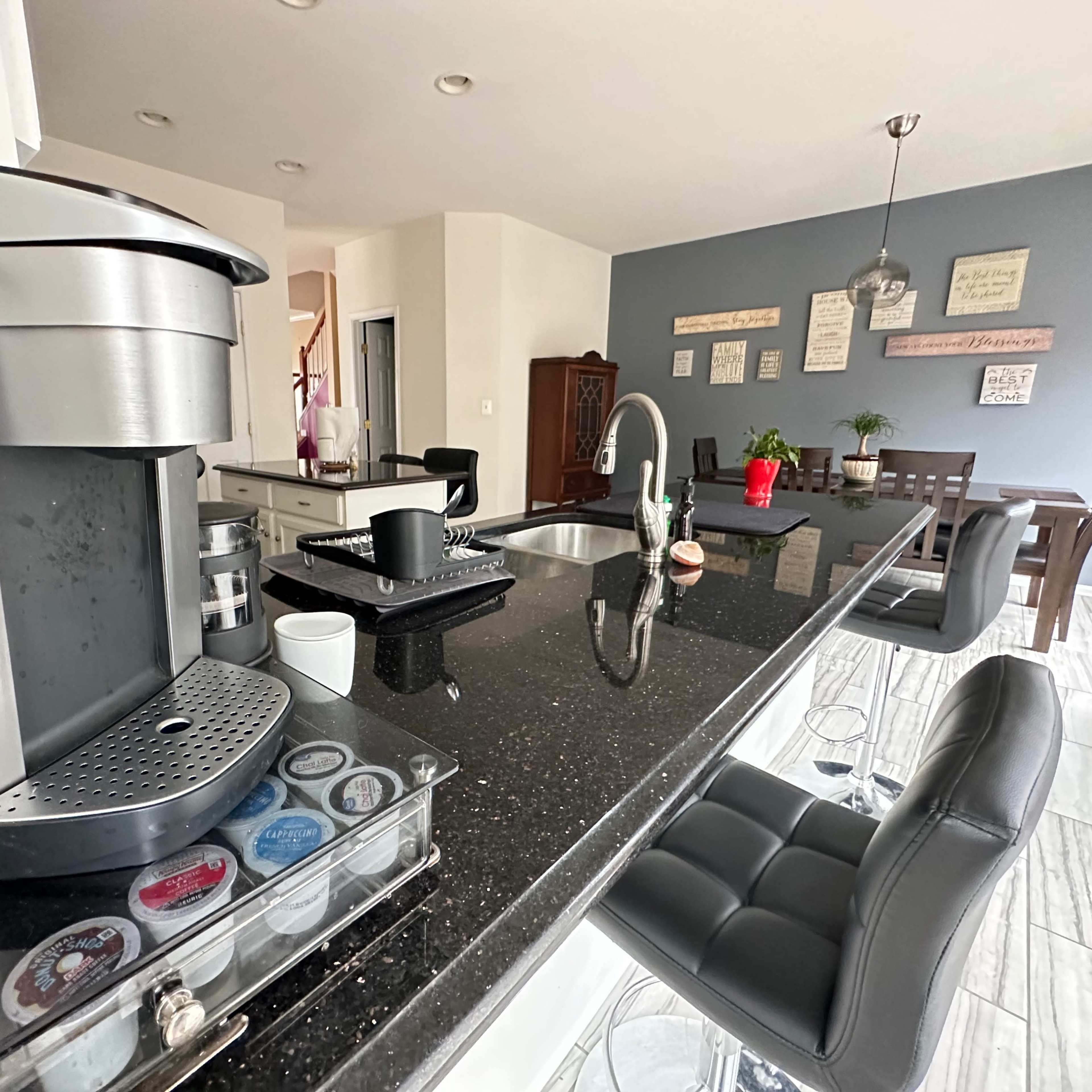 The kitchen features a coffee maker on the counter, a dining area with a table in the background, and a blend of dark and light-colored cabinetry.
