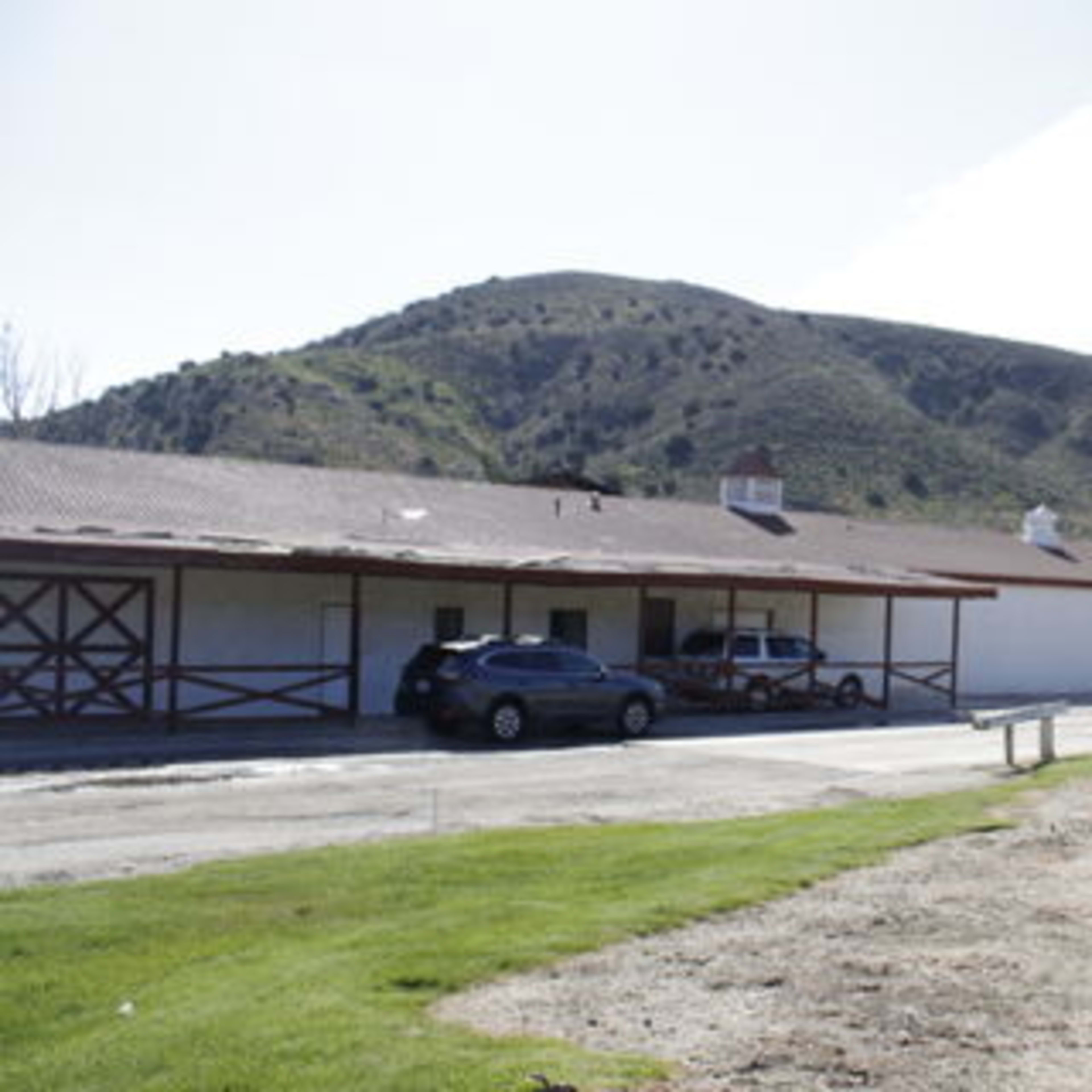 A rural landscape with a row of buildings adjacent to a dirt road, set against a backdrop of green hills.