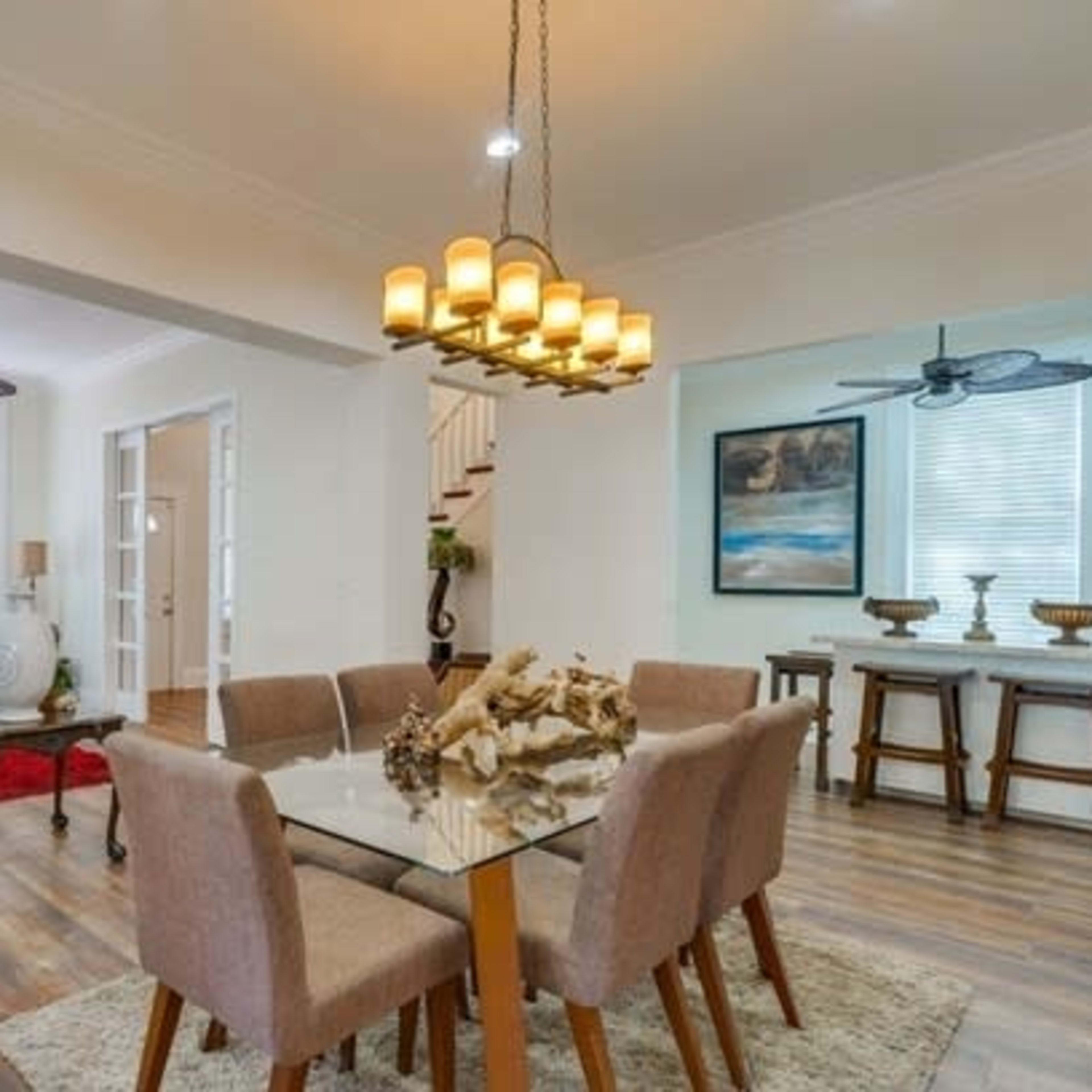 A modern living and dining area featuring a glass dining table, beige chairs, a comfortable sofa, and decorative lighting.